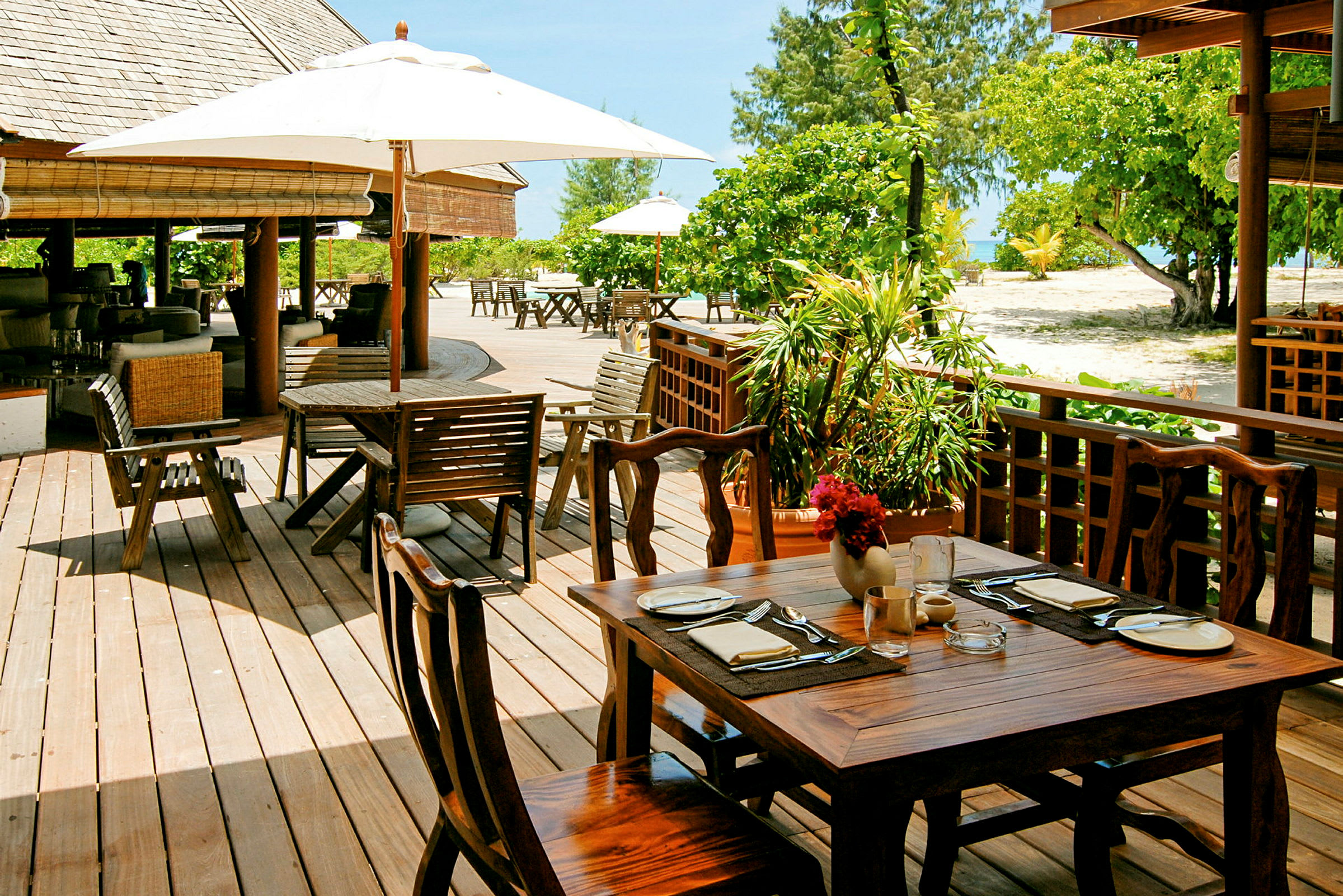 Udendørs restaurant med træborde og stole under parasoller, omgivet af grønt. (AI-genereret tekst)