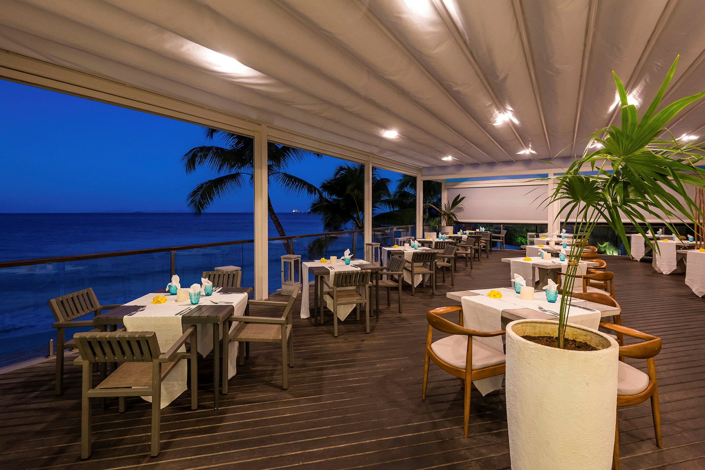 En udendørs servering ved havet med dækkede borde under en overdækket terrasse. (AI-genereret tekst)