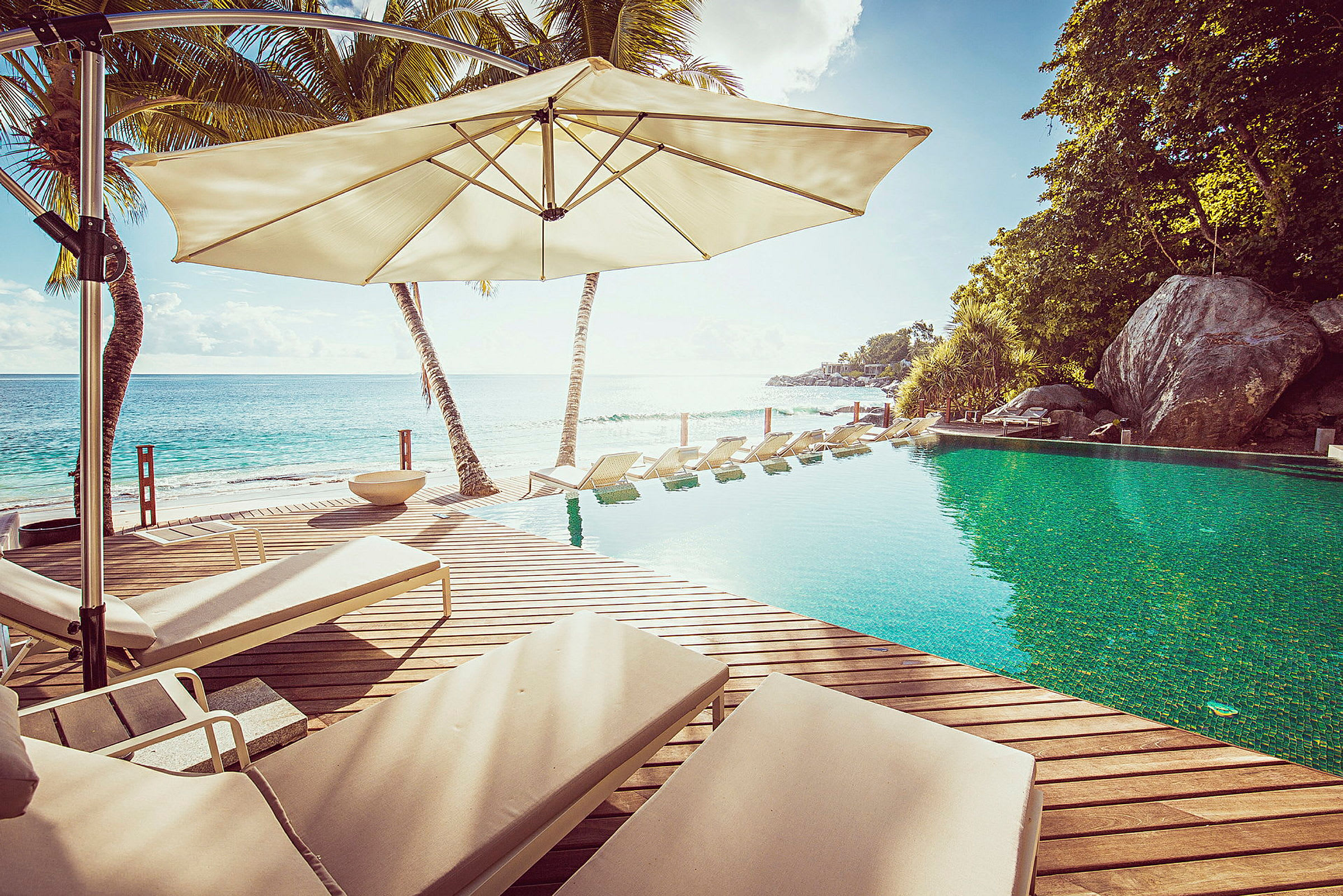 En pool ved stranden med liggestole under parasoller. (AI-genereret tekst)
