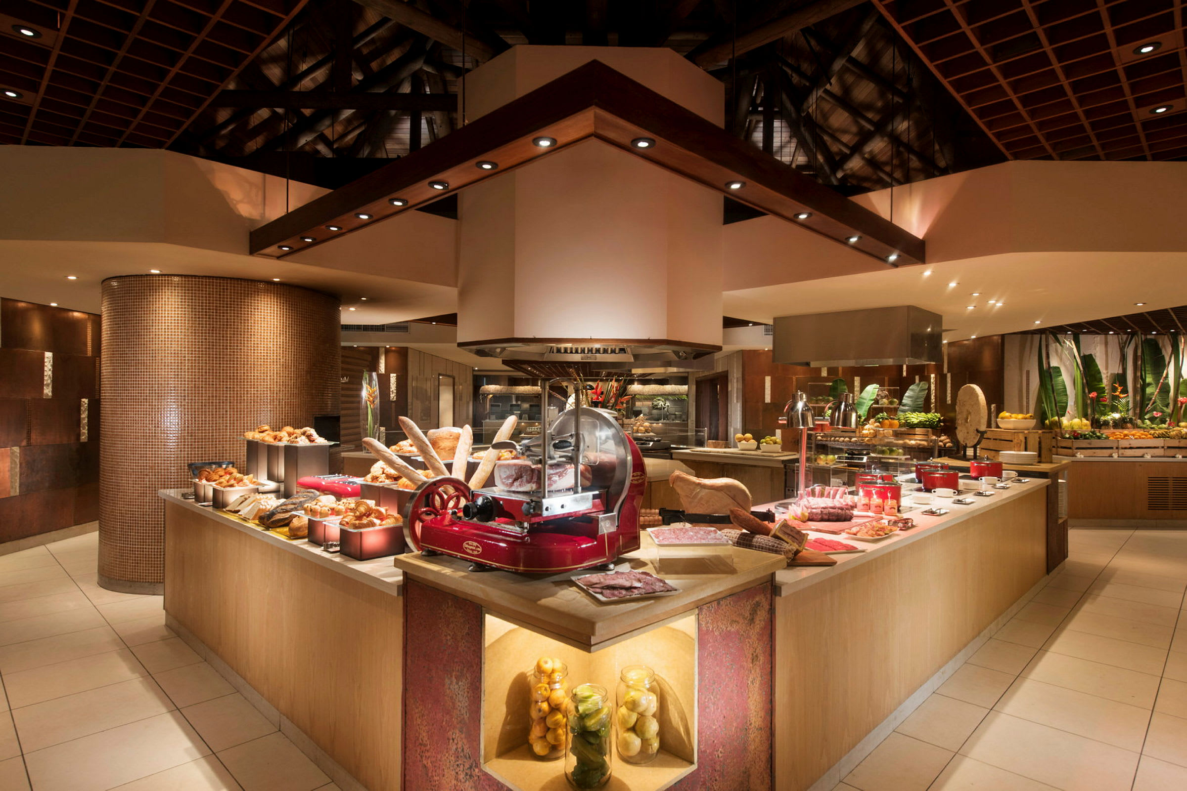 Billede af en godt oplyst buffet med forskellige slags mad som brød og frugt samt skæremaskine i centrum. (AI-genereret tekst)