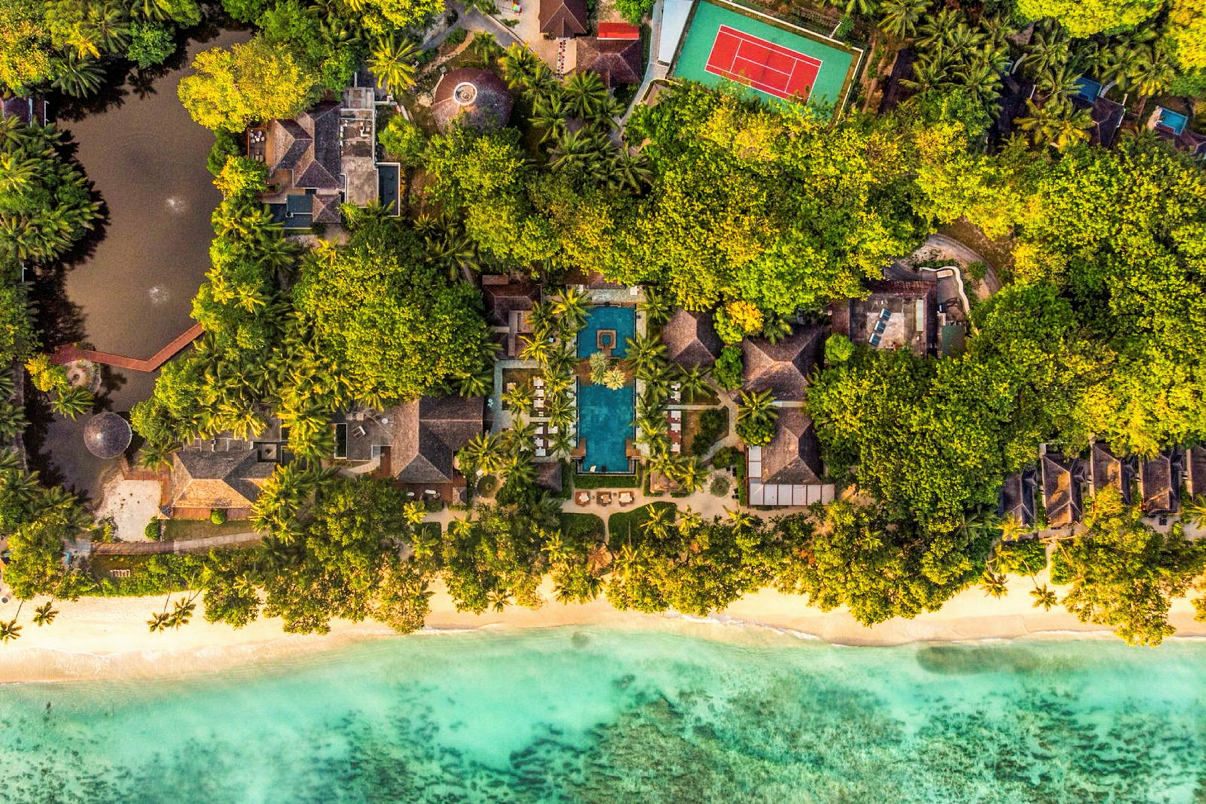 Luftfoto af en tropisk resort med frodig vegetation, swimmingpool, strand og turkis hav. (AI-genereret tekst)