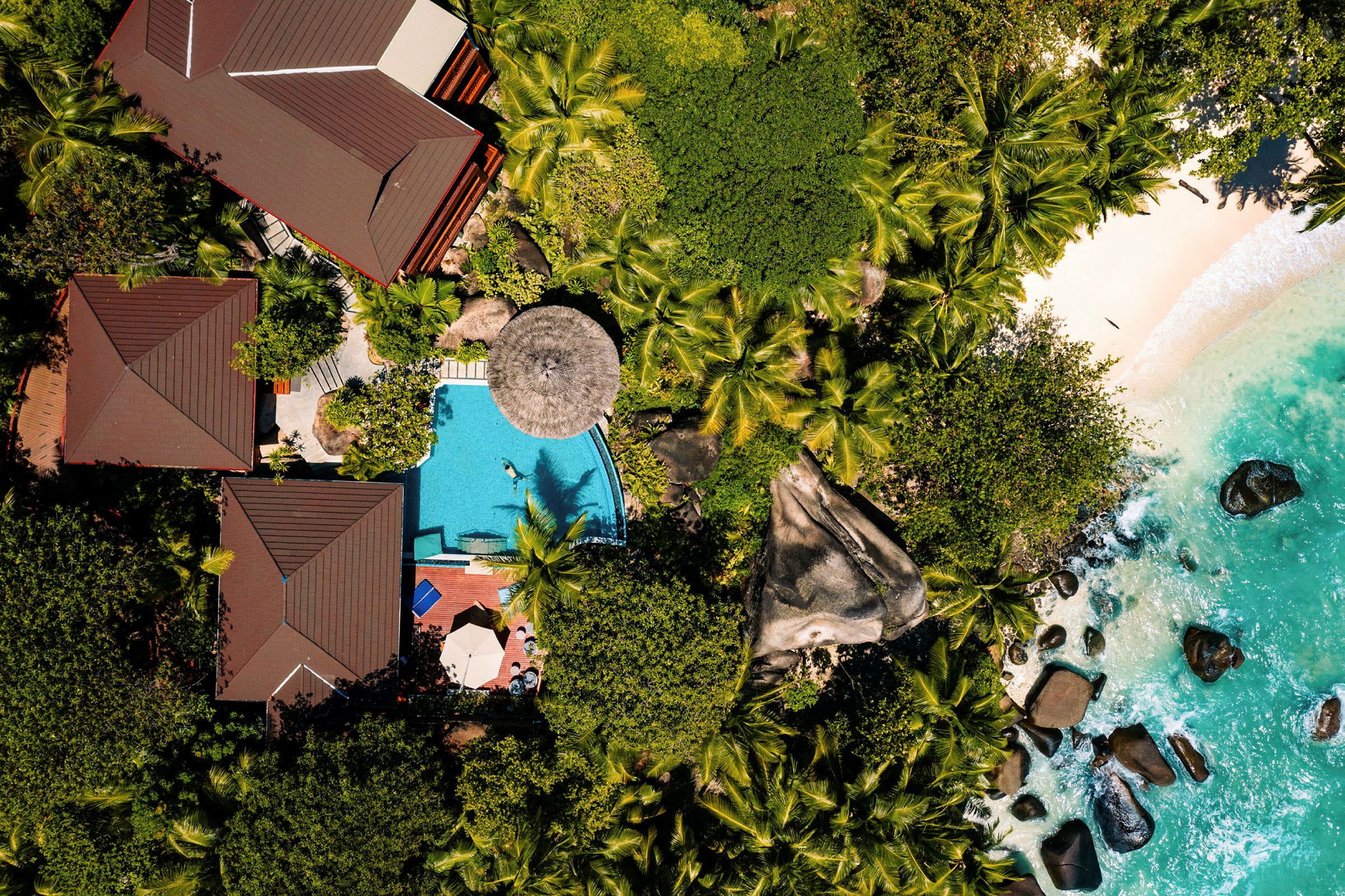 Luftfoto af tropisk resort med pool, strand og frodig vegetation. (AI-genereret tekst)