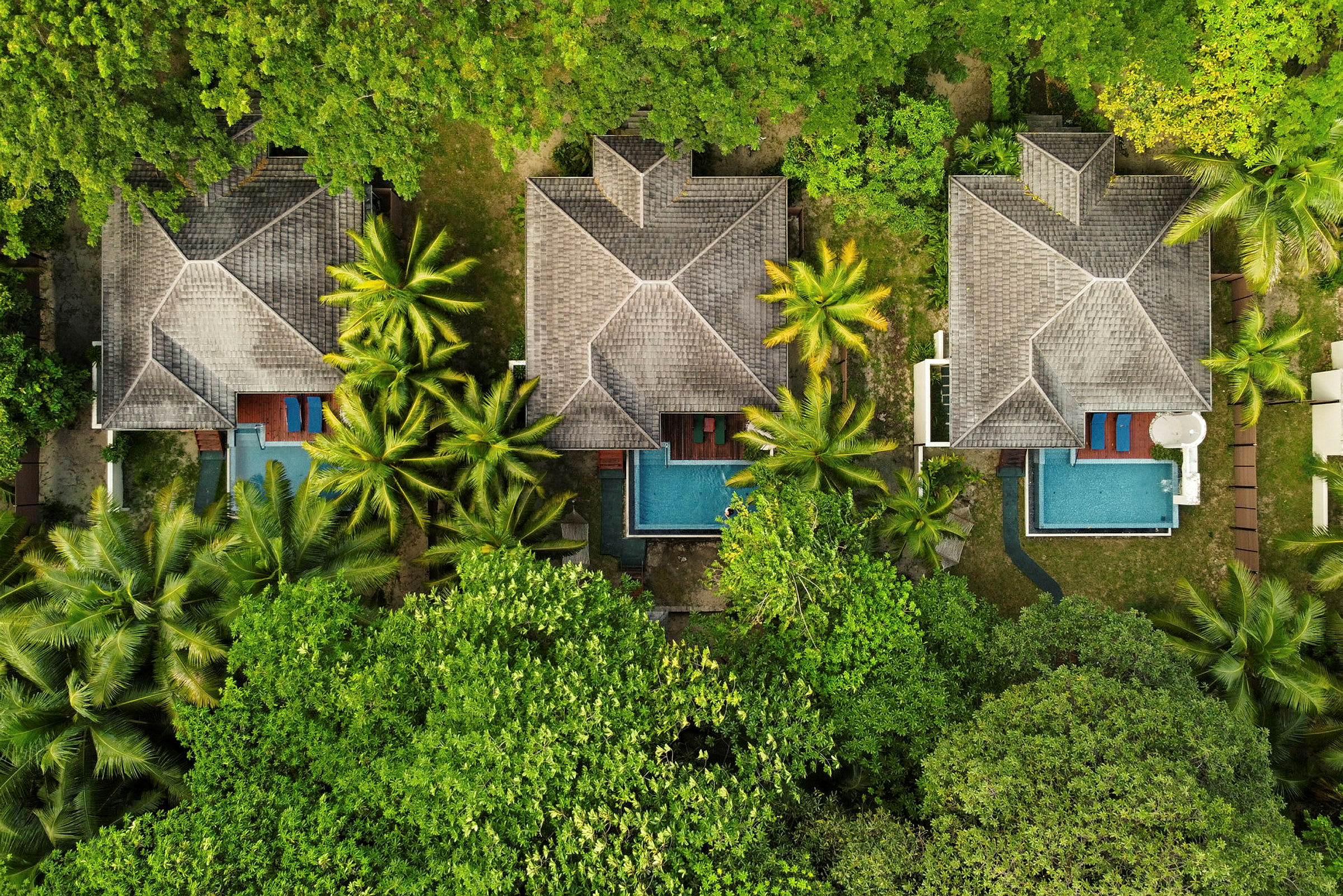 Luftfoto af tre bungalower med swimmingpools omgivet af grønne områder. (AI-genereret tekst)