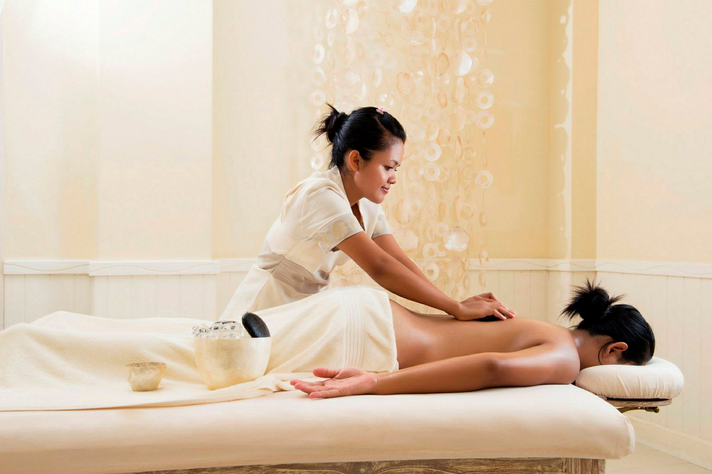 En massør udfører en rygmassage på en person, der ligger på en massagebriks i et spa. (AI-genereret tekst)