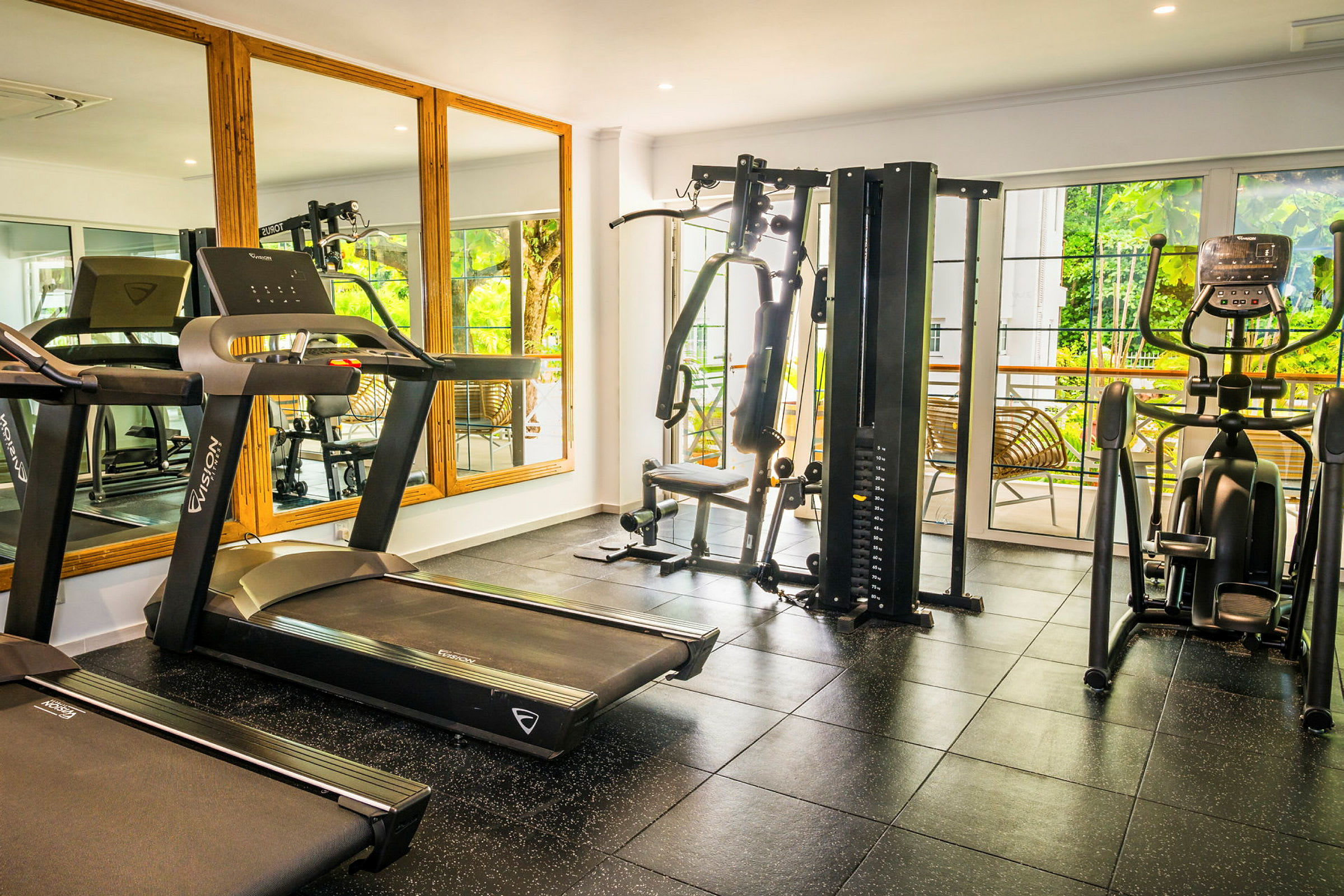 Et fitnesscenter med forskellige træningsmaskiner, herunder løbebånd, multigym og motionscykel. Bag træningsmaskinerne er der store vinduer og spejle. (AI-genereret tekst)