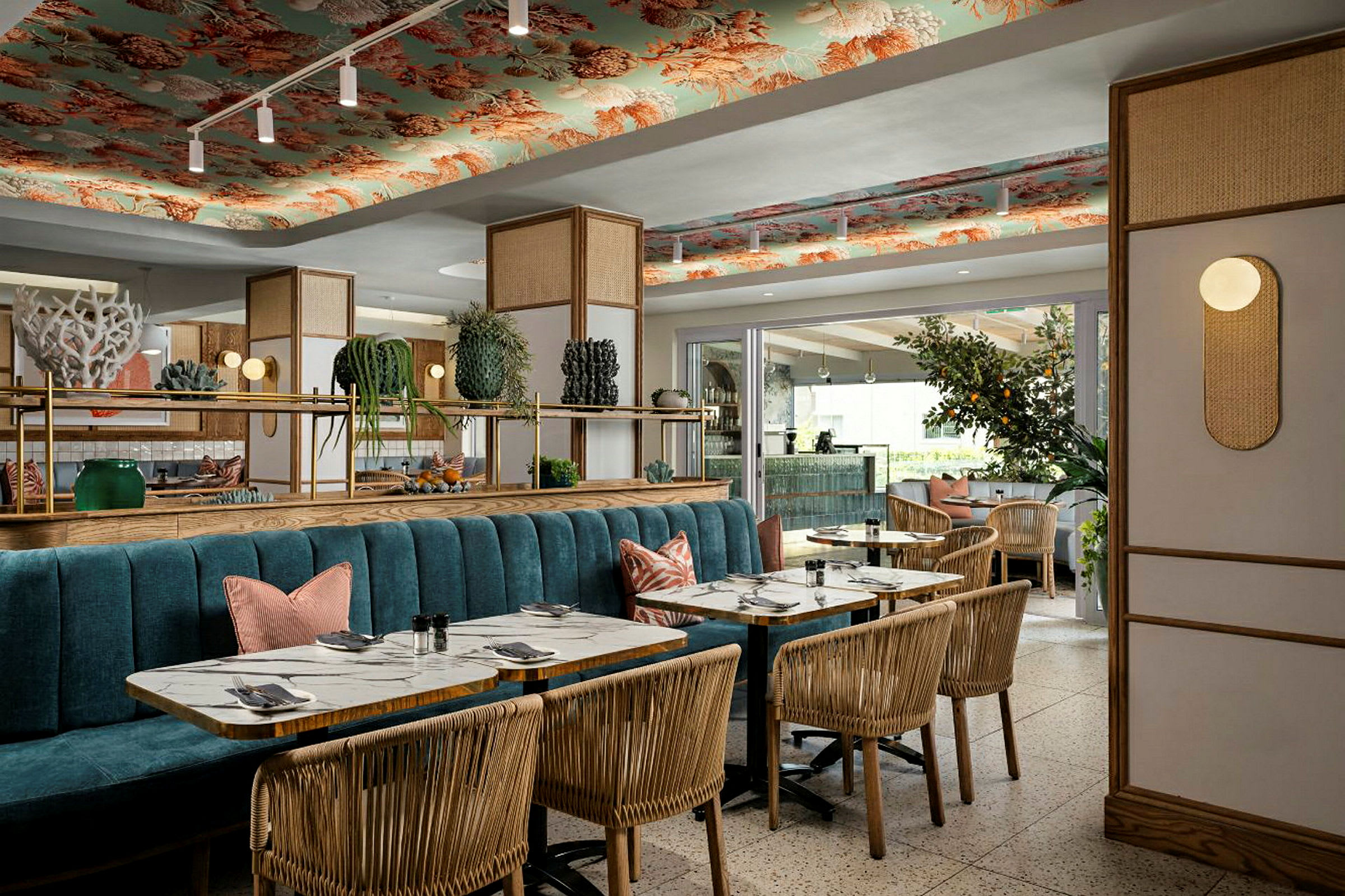 Et elegant restaurantinteriør med træstole, marmorborde og en blå sofabænk. Loftet er dekoreret med mønstre, og indretningen suppleres med planter og belysning. (AI-genereret tekst)