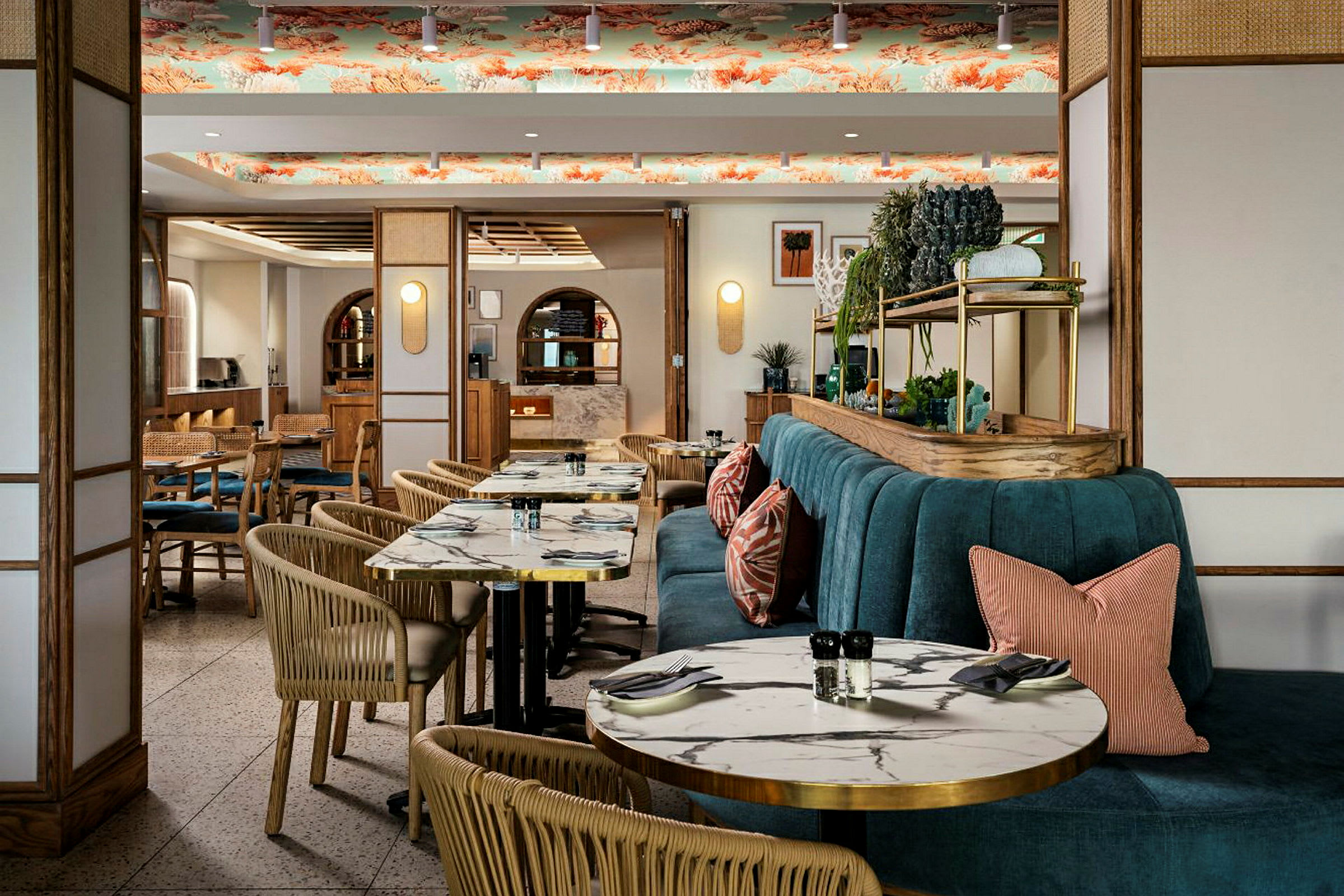 En restaurantindretning med marmorerede borde, kurvestole og en turkis bænk med puder. Loftet har dekorativt mønster. (AI-genereret tekst)
