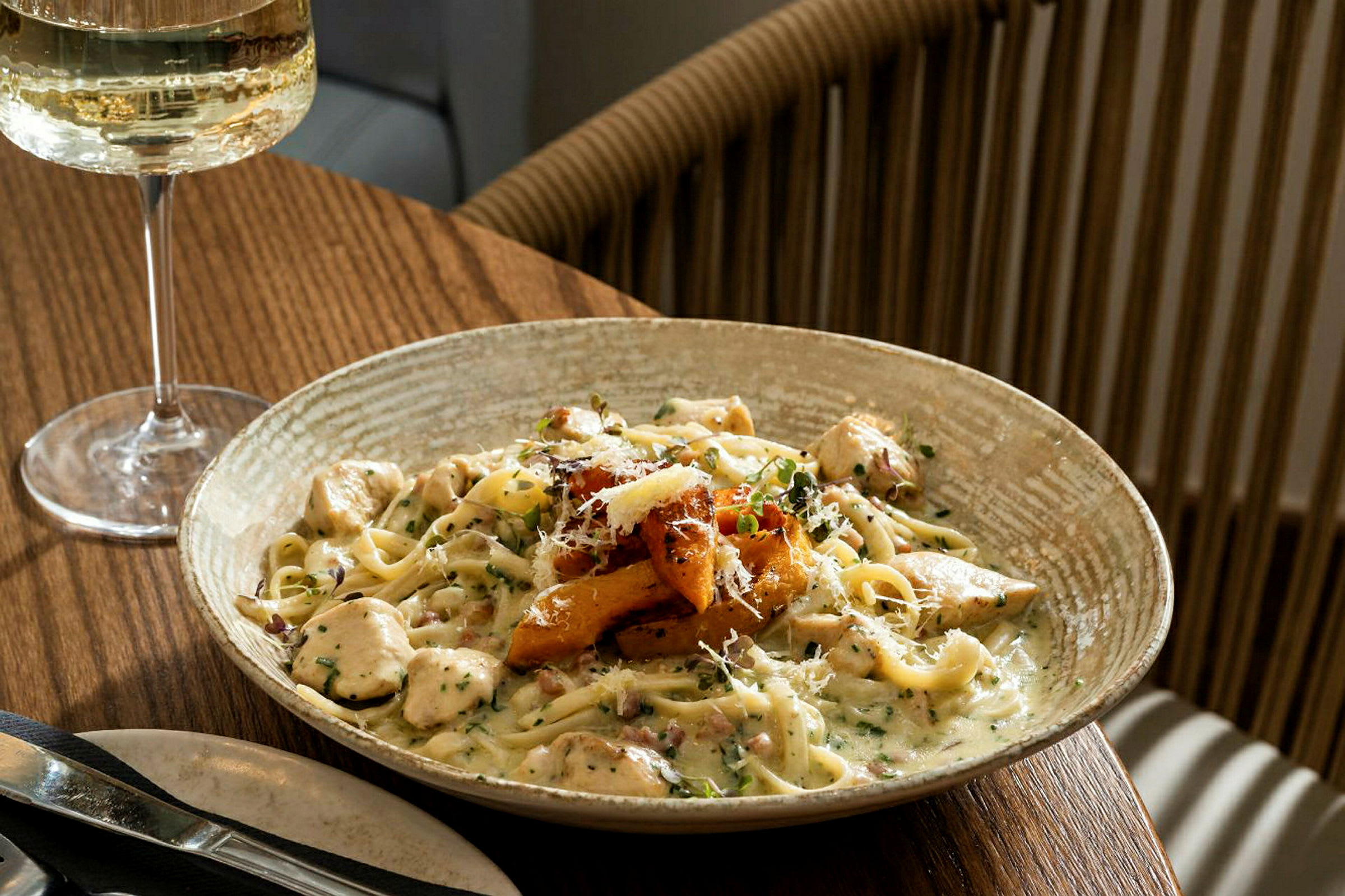 En tallerken med pasta med cremet sauce og tilbehør, serveret på et spisebord med et glas hvidvin. (AI-genereret tekst)