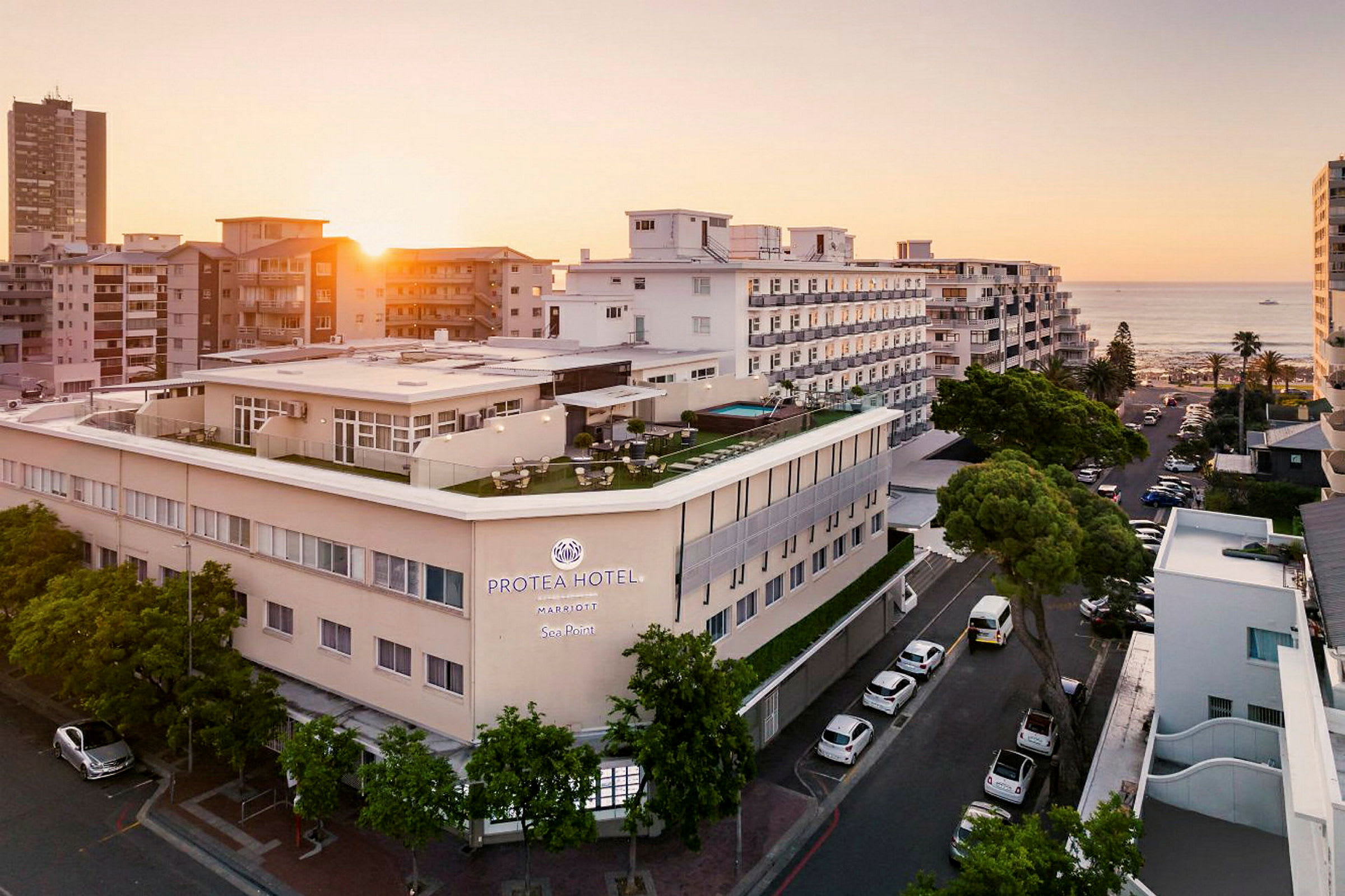 Hotelbygning ved havet omgivet af andre bygninger i solnedgang. (AI-genereret tekst)