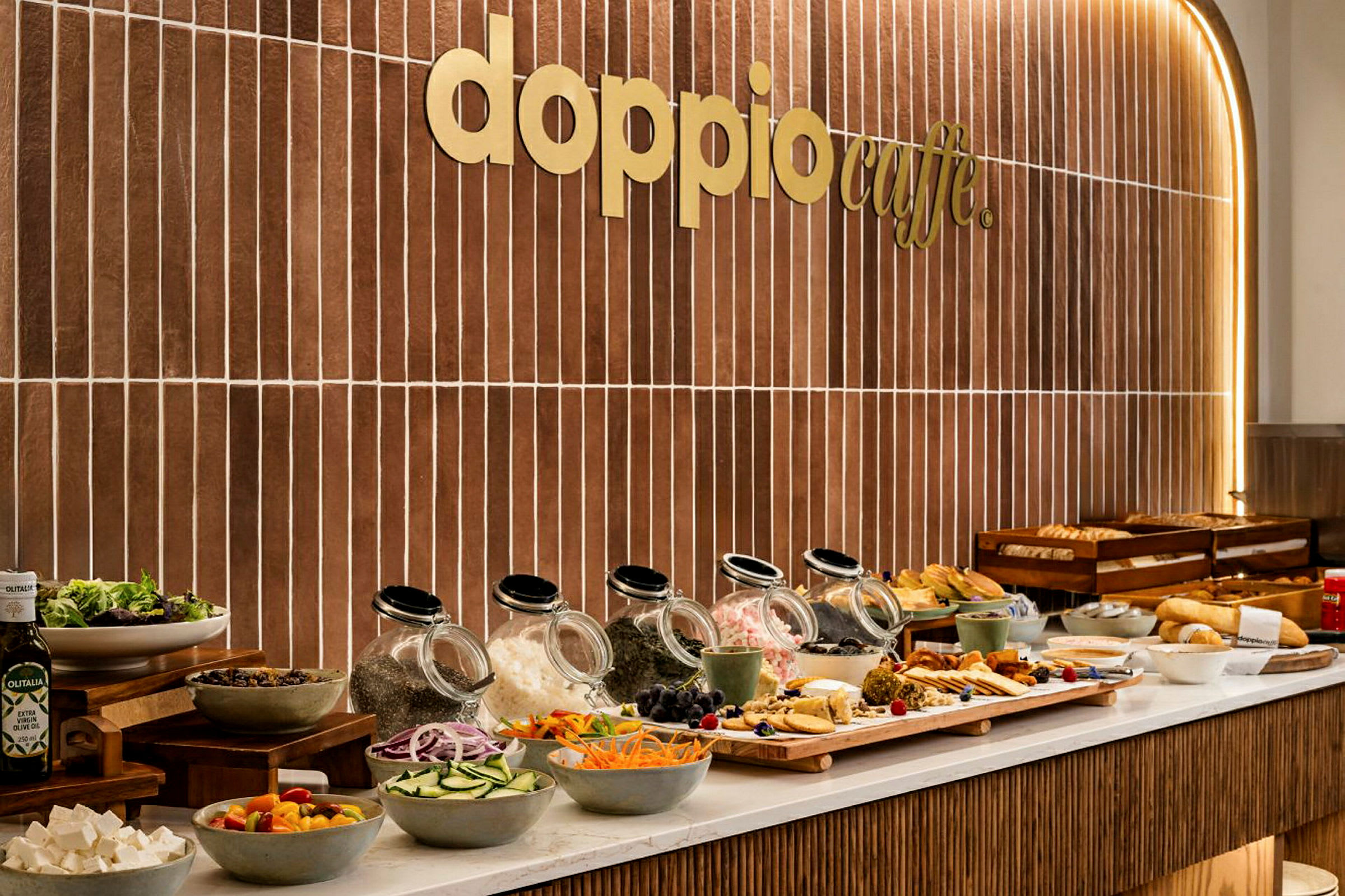 Billede af en buffet med forskellige fødevarer og salatingredienser foran en væg med teksten "Doppio Caffe". (AI-genereret tekst)