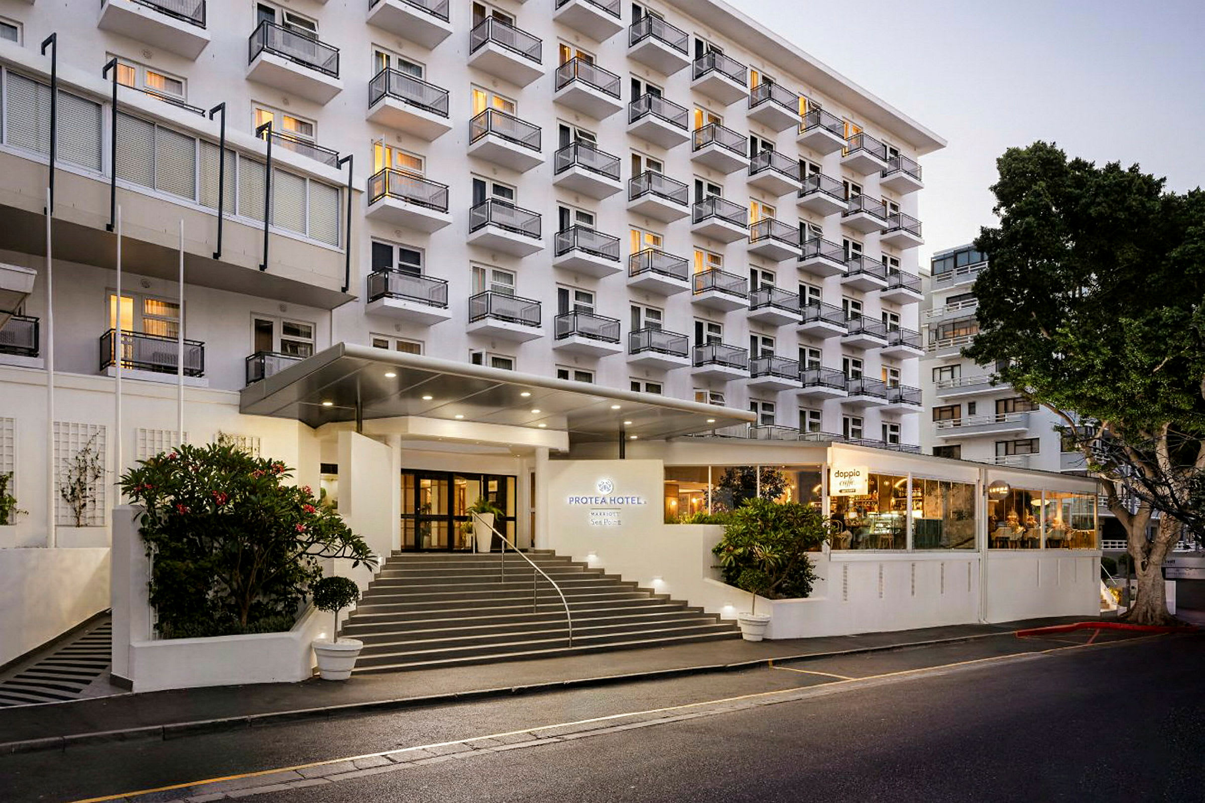Hotelbygning med flere etager og altaner, samt en oplyst indgang og trappe foran. (AI-genereret tekst)