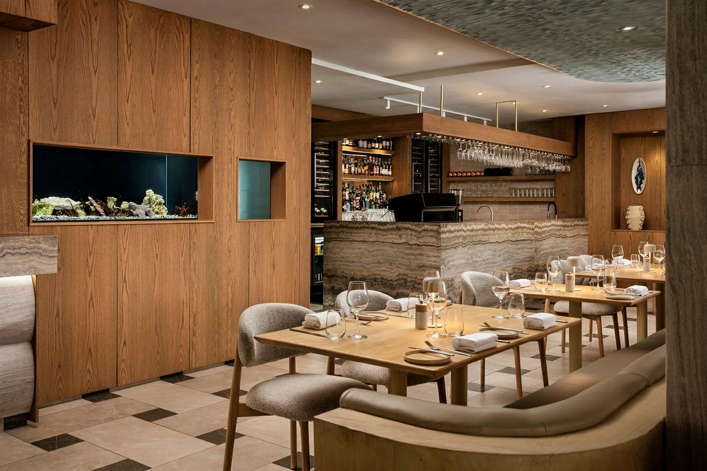 Et elegant restaurantinteriør med træmøbler og en bardisk i marmordesign. Bordene er dækket med glas og servietter. (AI-genereret tekst)