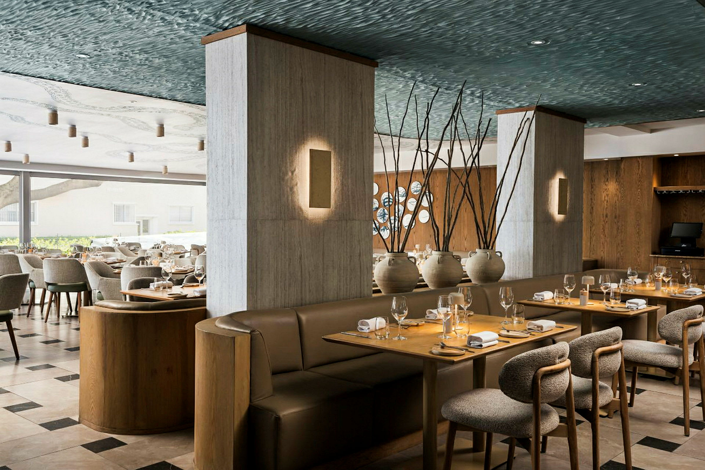 En elegant restaurantindretning med dækkede borde, polstrede stole og hyggelige sofaer. Dekorationer inkluderer keramikvaser og træelementer. (AI-genereret tekst)