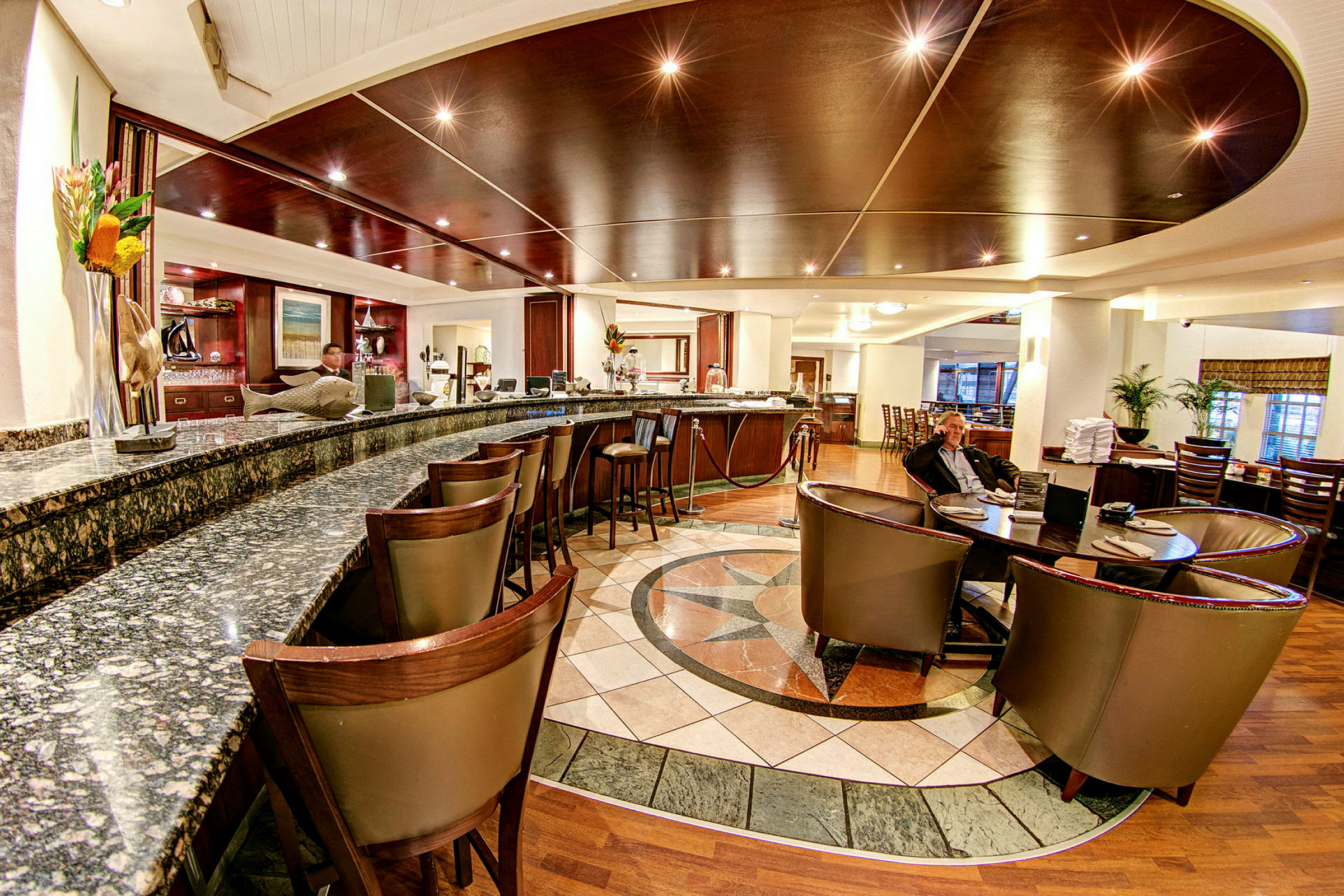 Et elegant hotelbarområde med marmordisk, mørke træmøbler og loungeområde. (AI-genereret tekst)