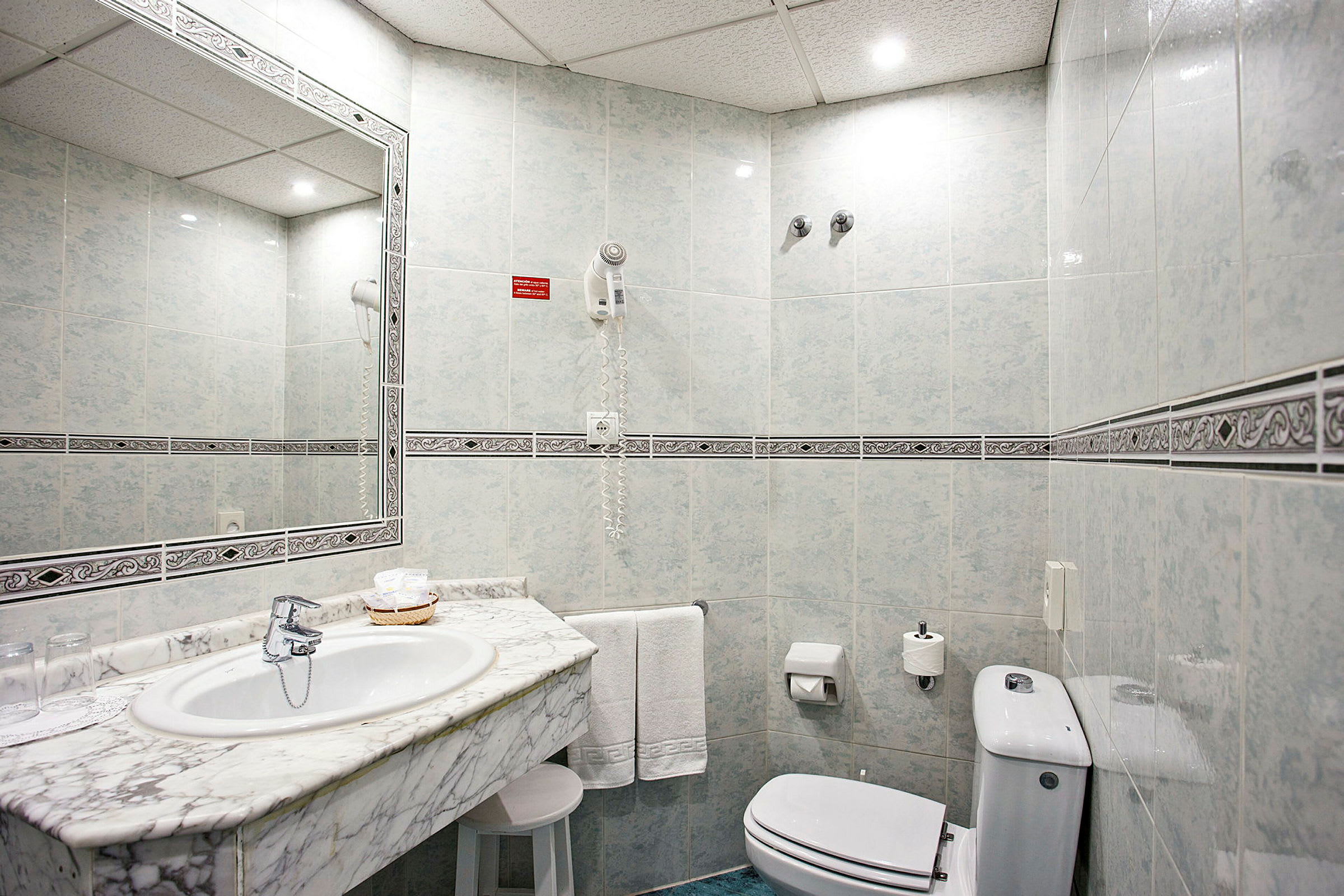 Badeværelse med marmoreret håndvask, spejl, toilet og håndklæder. (AI-genereret tekst)