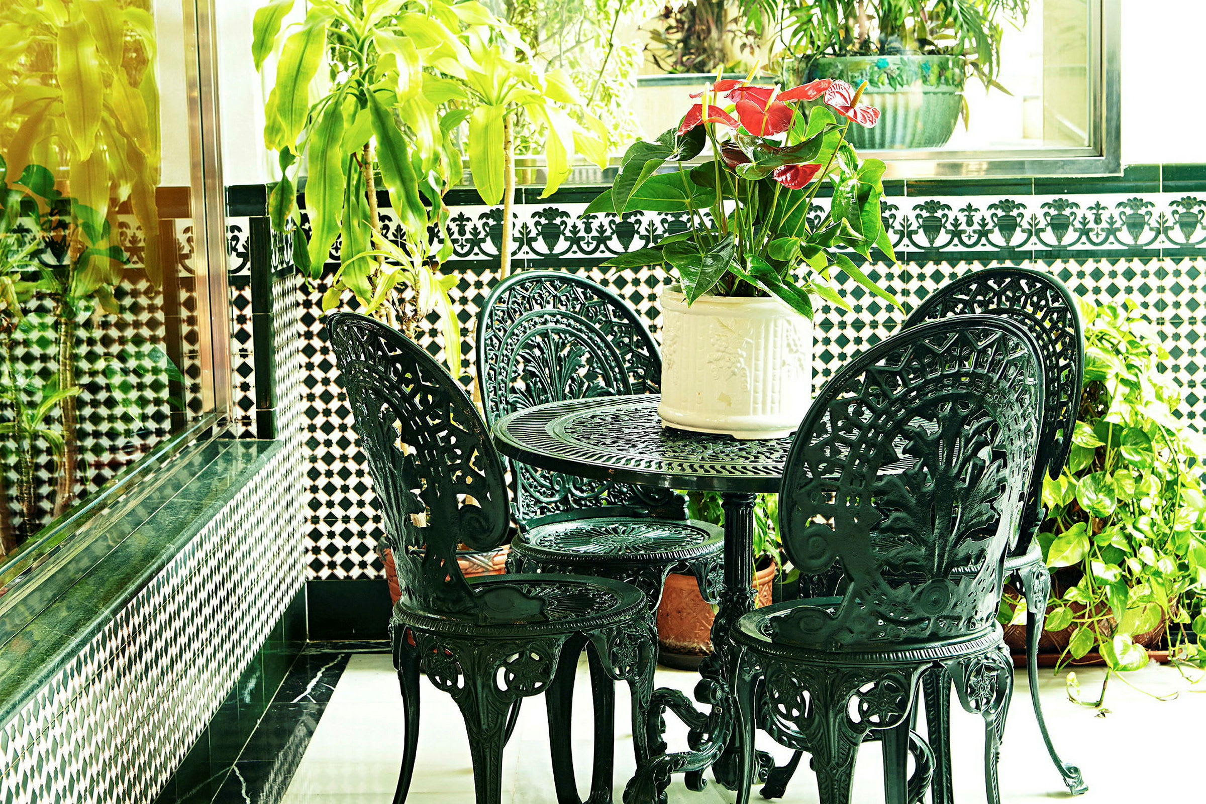 En lille terrasse med et sort jernbord og stole, dekoreret med planter og blomster. (AI-genereret tekst)