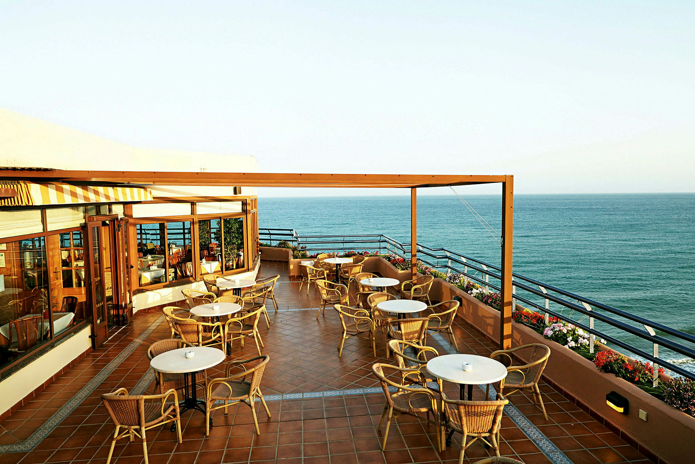 En terrasse med borde og stole og udsigt over havet. (AI-genereret tekst)