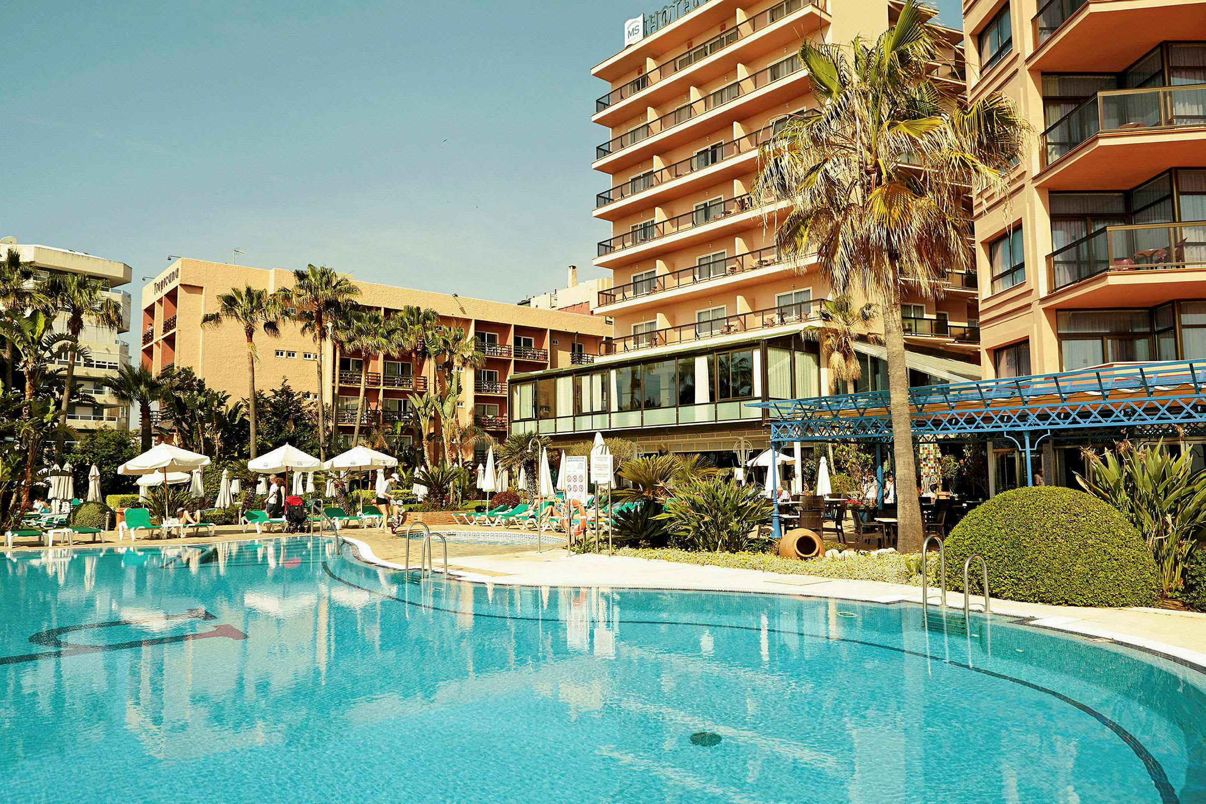 Et hotel med en pool og palmer. (AI-genereret tekst)