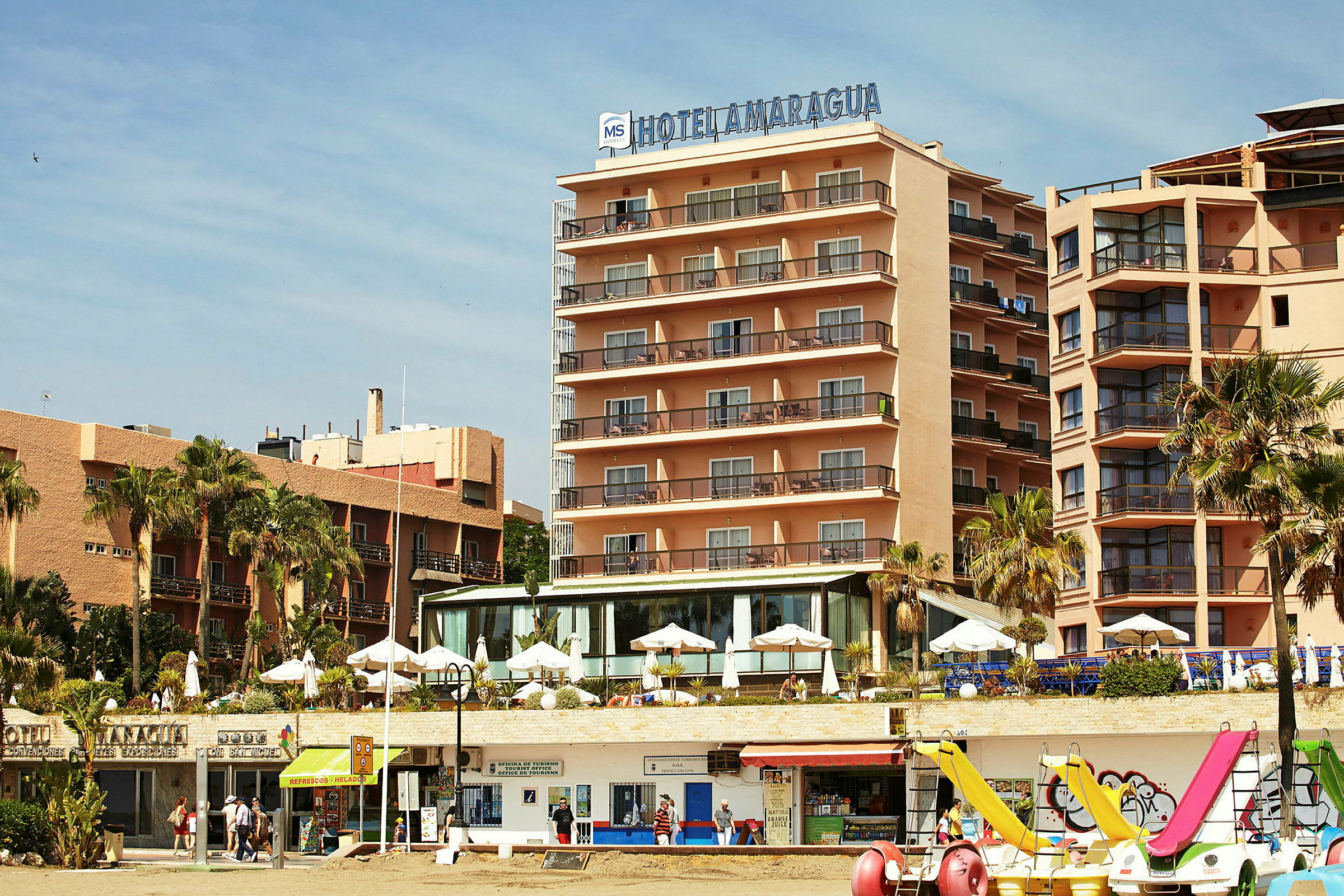 Et hotel beliggende ved stranden med parasoller og udsigt til havet. (AI-genereret tekst)
