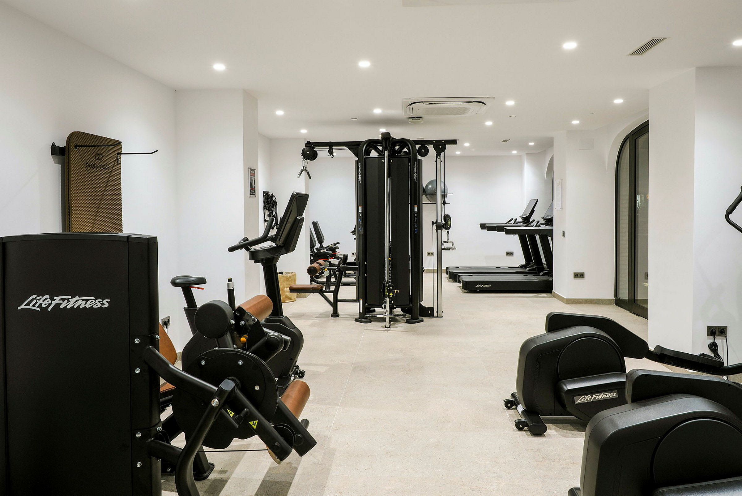 Et fitnesscenter med træningsmaskiner og løbebånd placeret i et lyst rum. (AI-genereret tekst)