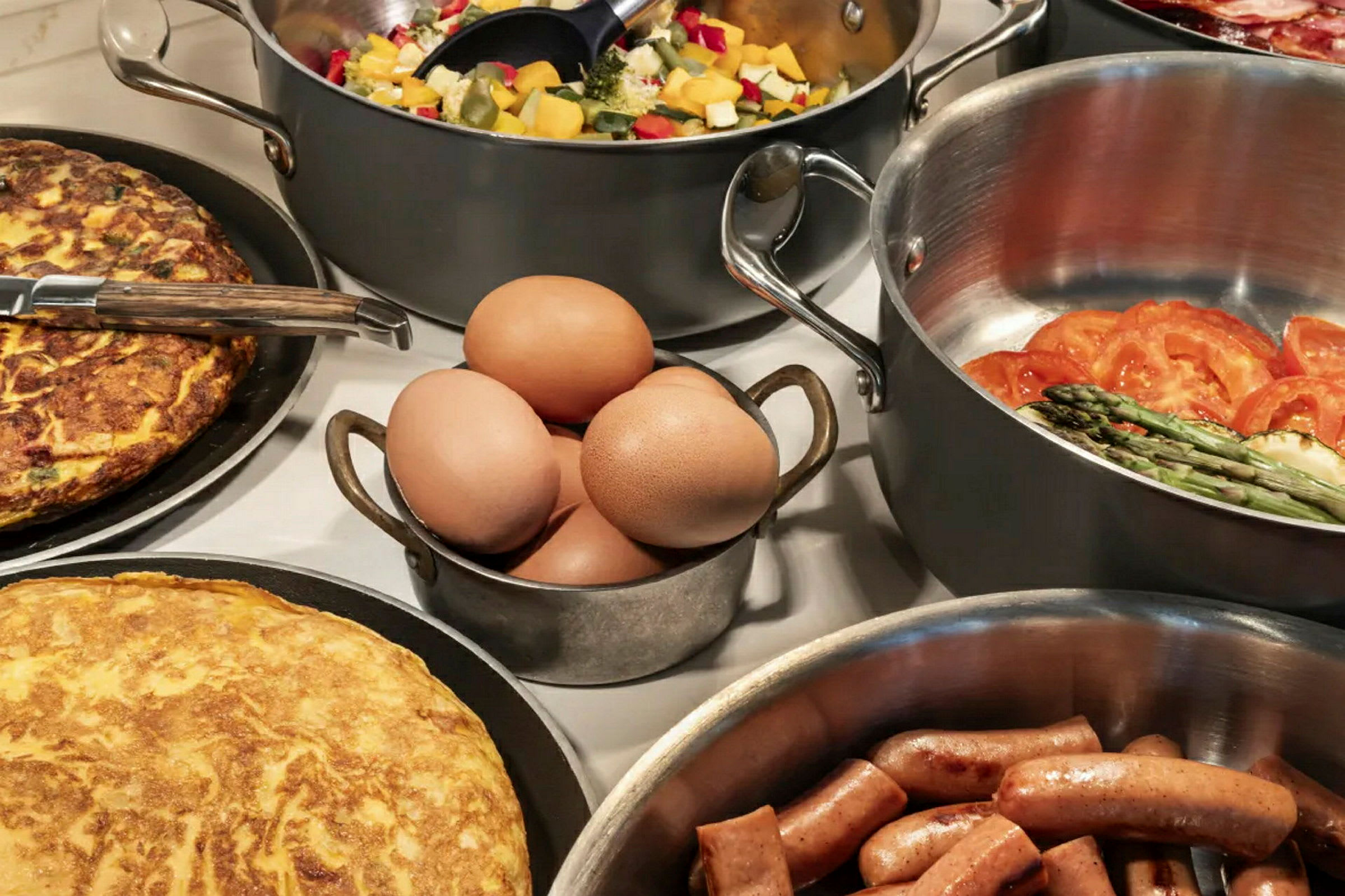 Forskellige retter, herunder omelet, pølser, æg og grøntsager, arrangeret på et bord. (AI-genereret tekst)