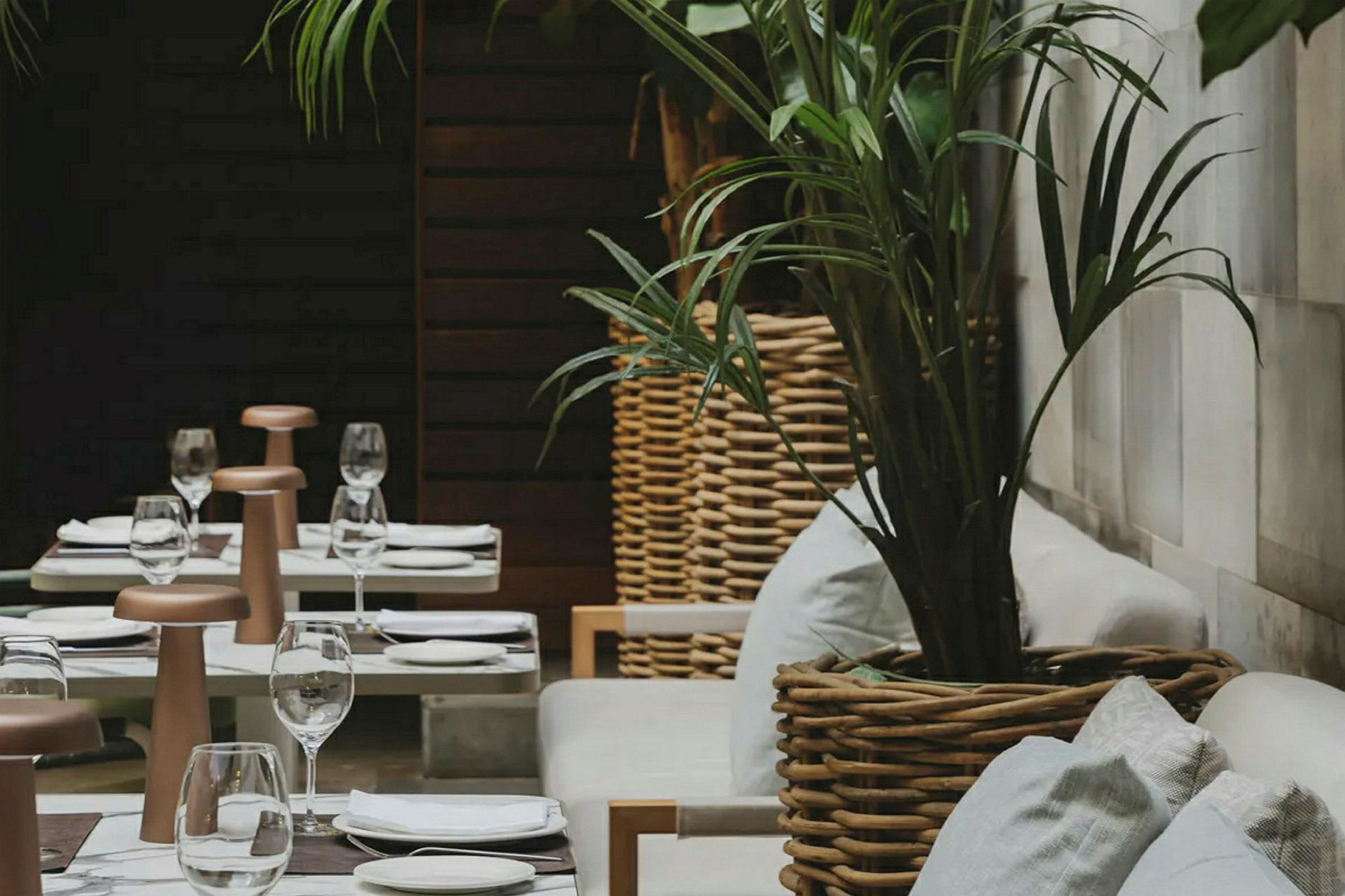 En terrasse med opdækkede borde og komfortable stole omgivet af planter i flettede kurvkrukker. (AI-genereret tekst)