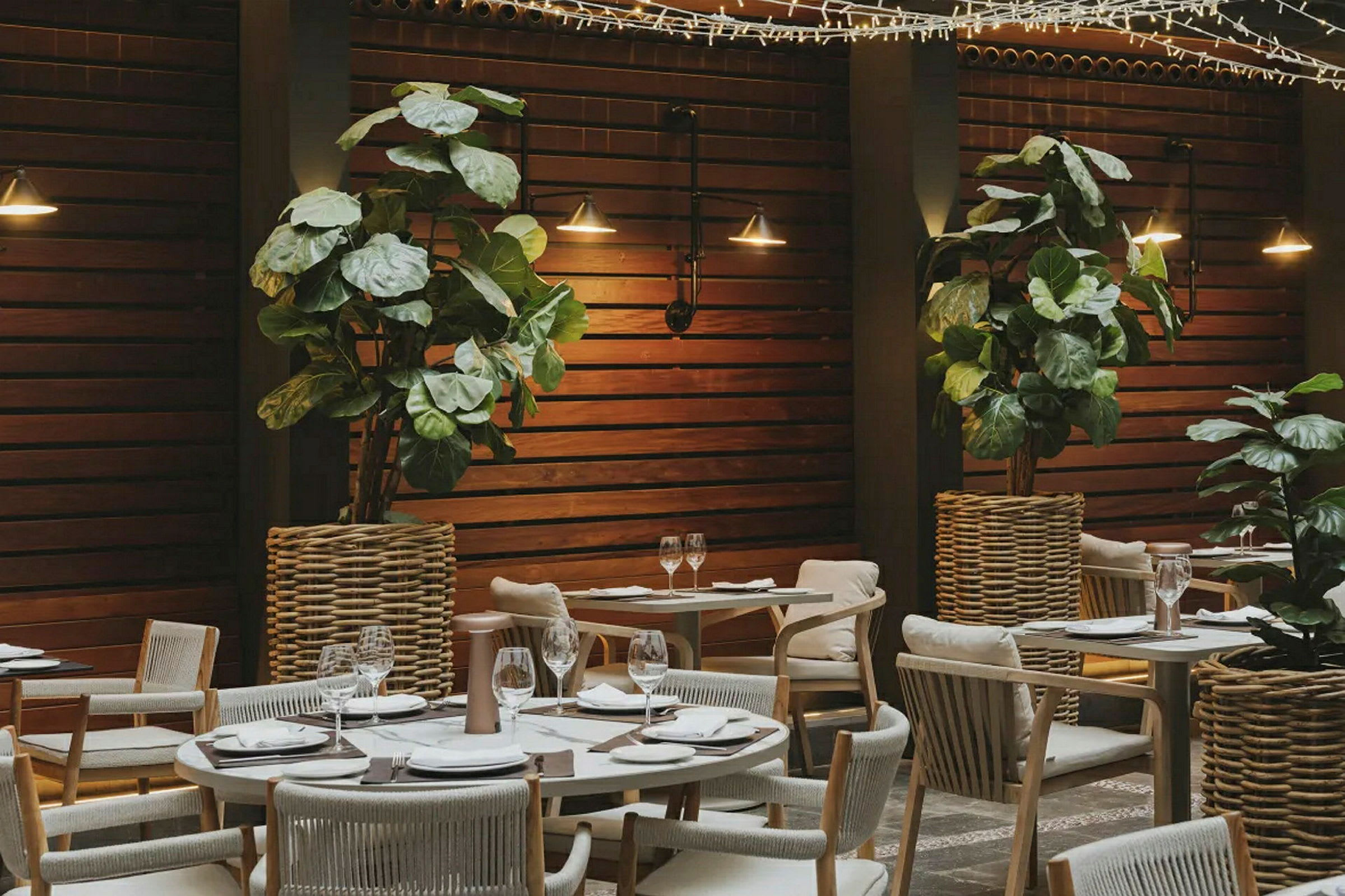 En oplyst restaurant med træpaneler, plantepynt og dækkede borde. (AI-genereret tekst)