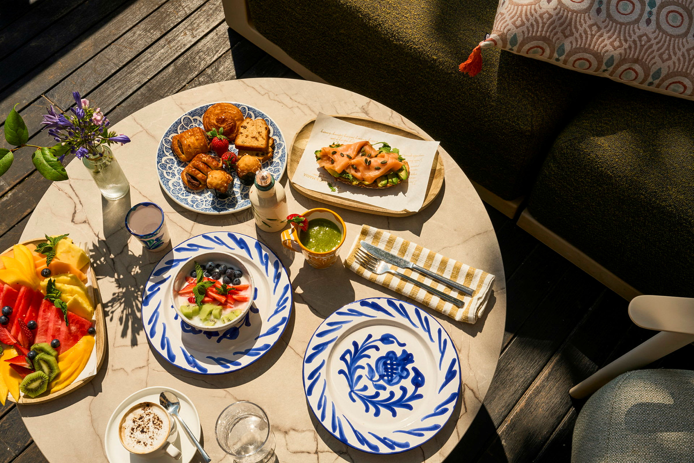 Et marmorbord med et udvalg af farverige retter, morgenmad og dekorative tallerkener samt friske blomster. (AI-genereret tekst)