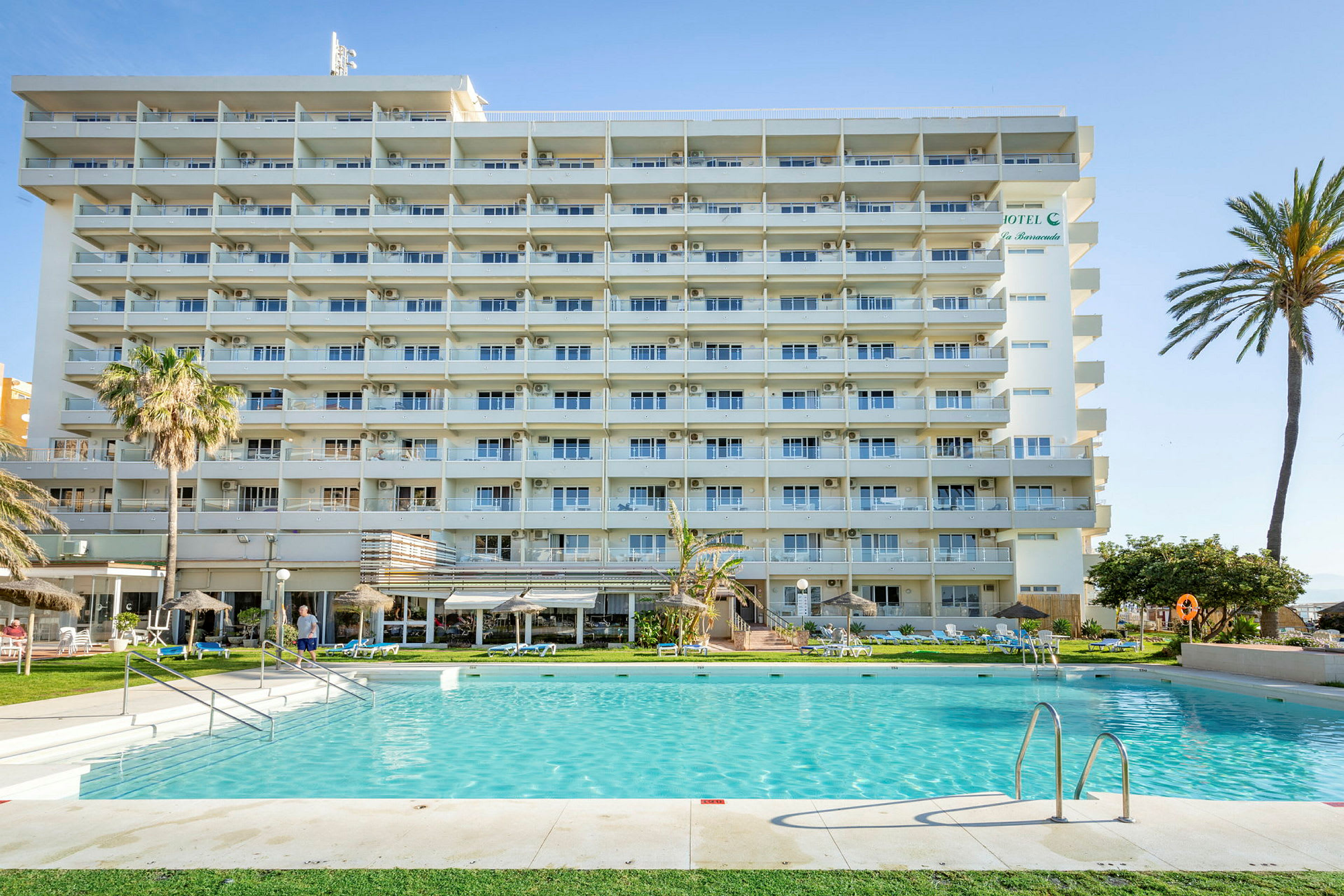 Et lejlighedshotel med altaner foran en swimmingpool og omkringliggende have. (AI-genereret tekst)