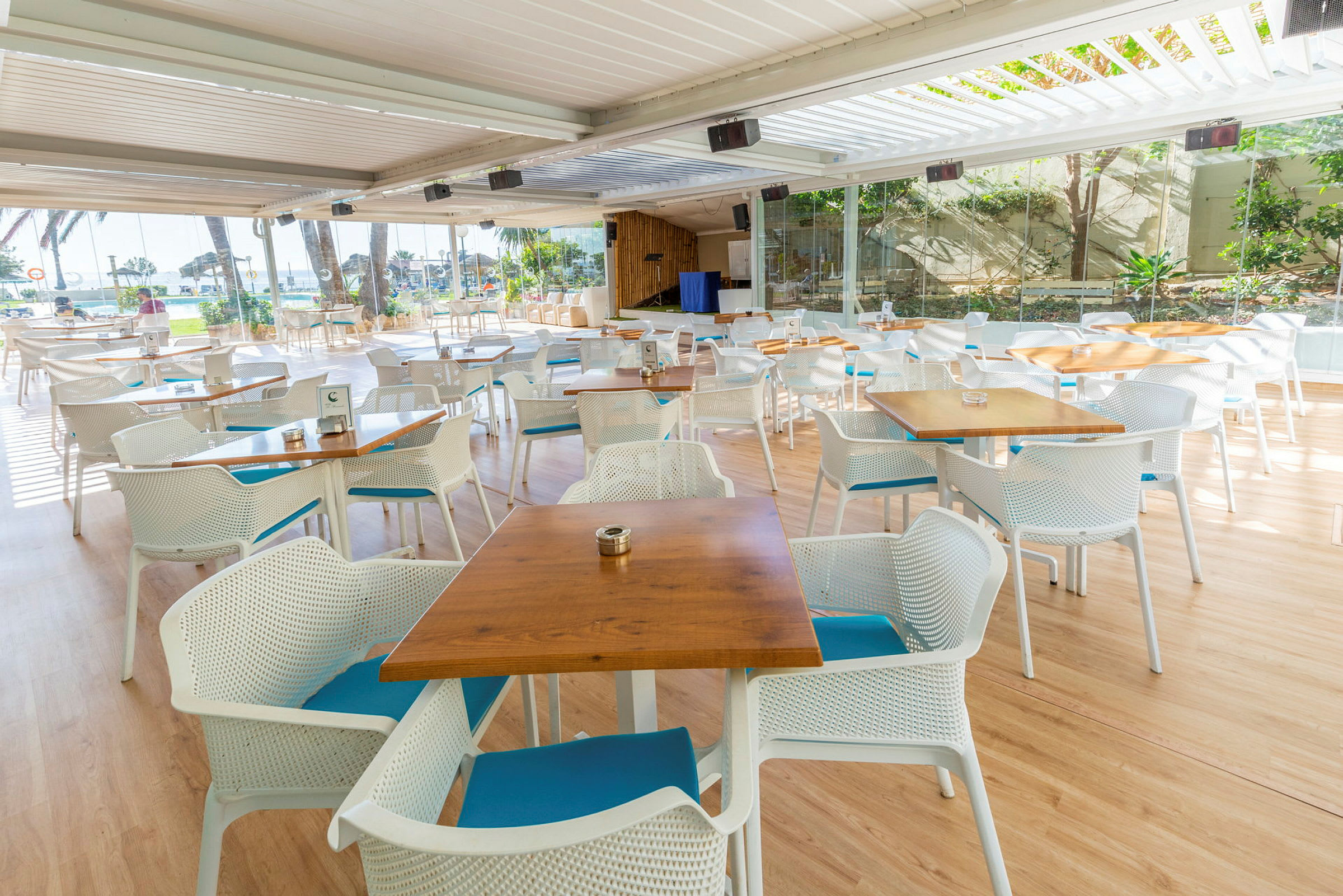 Udendørs restaurant med borde og stole foran panoramavinduer. (AI-genereret tekst)