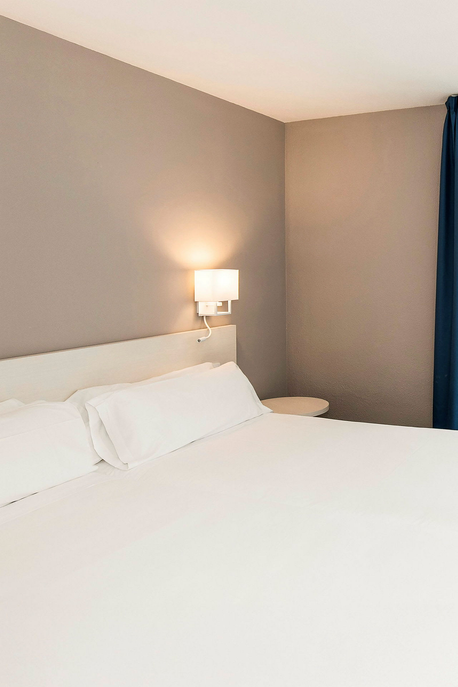 En hoteltseng med hvidt sengetøj og væglampe. (AI-genereret tekst)