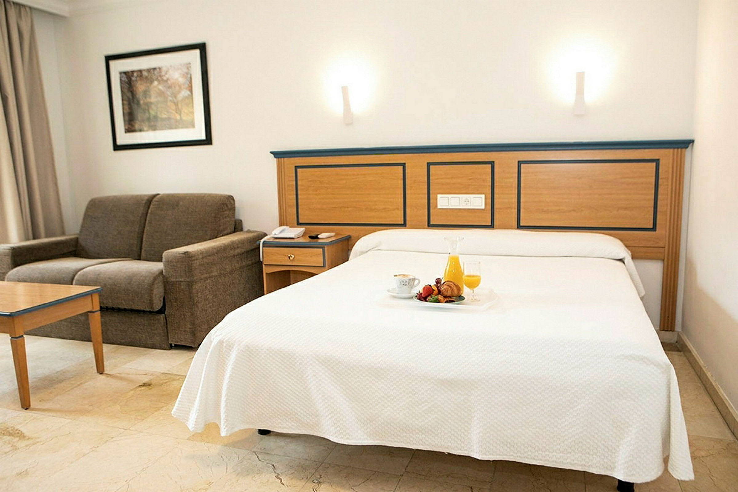 Hotelværelse med redt seng og sofa. (AI-genereret tekst)