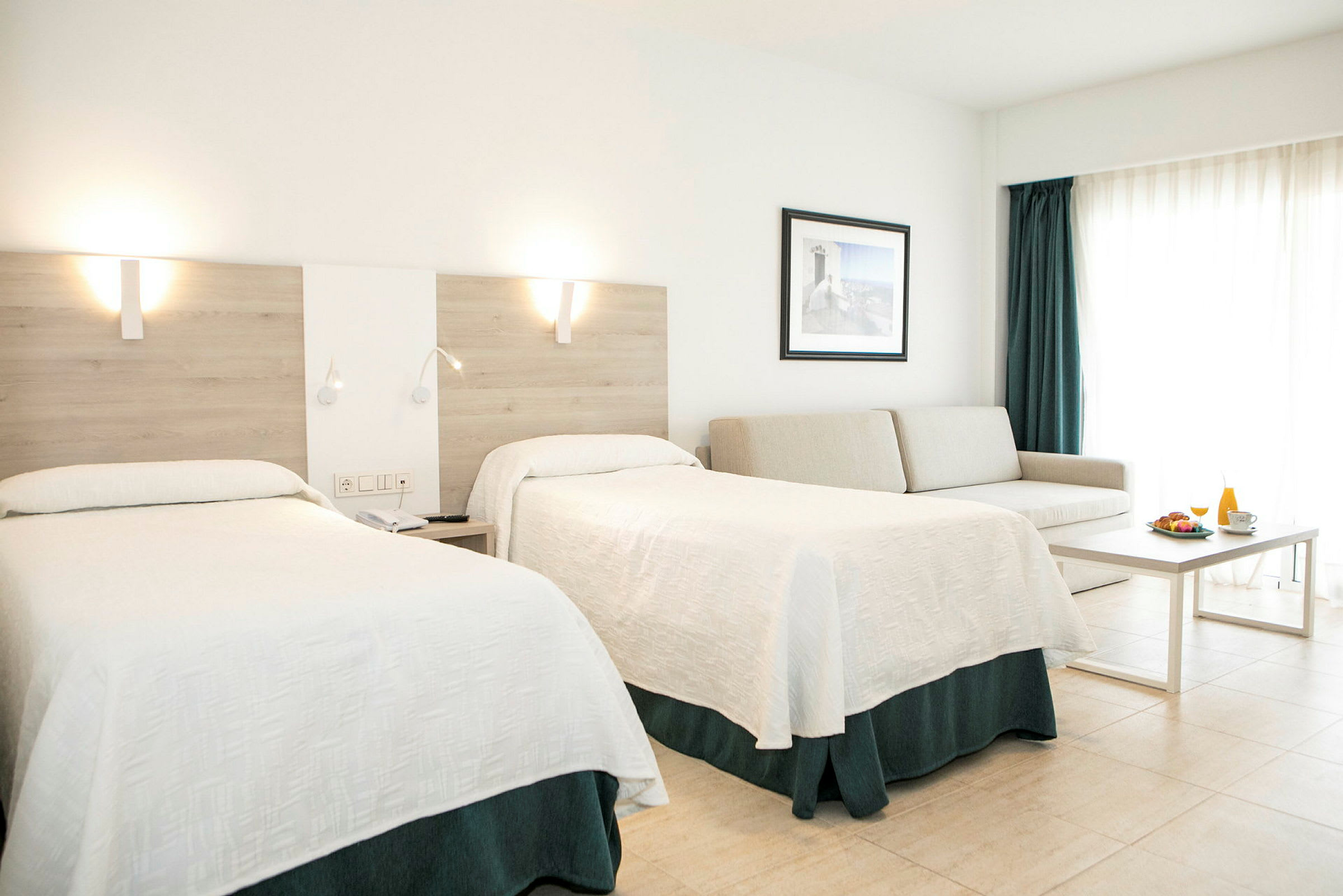 Et hotelværelse med to senge, en sofa, et bord og en morgenmadsservering. (AI-genereret tekst)