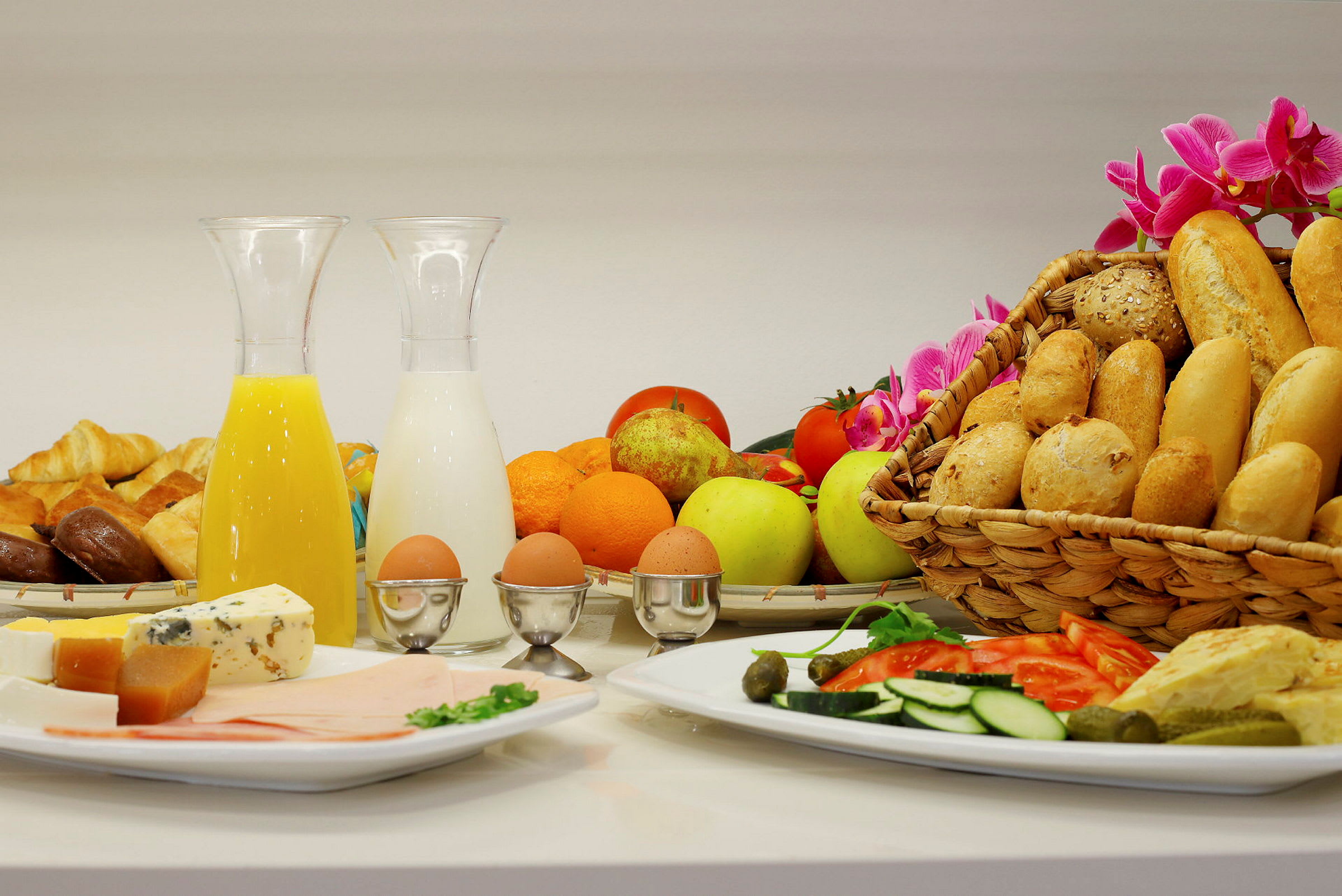 En morgenbuffet med forskellige brød, frugt, grøntsager, ost, pålæg, kogte æg samt drikkevarer som juice og mælk. (AI-genereret tekst)