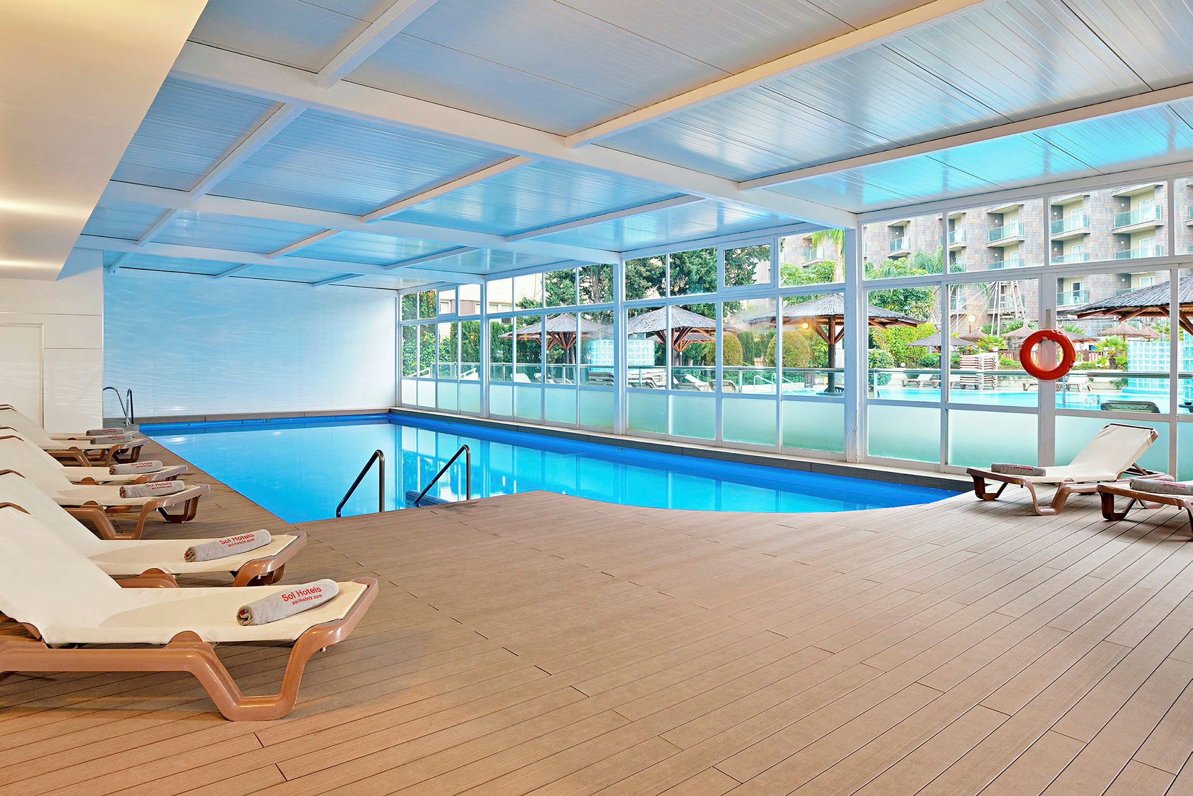Indendørs swimmingpool med solsenge langs kanten og udsigt gennem glasvægge. (AI-genereret tekst)