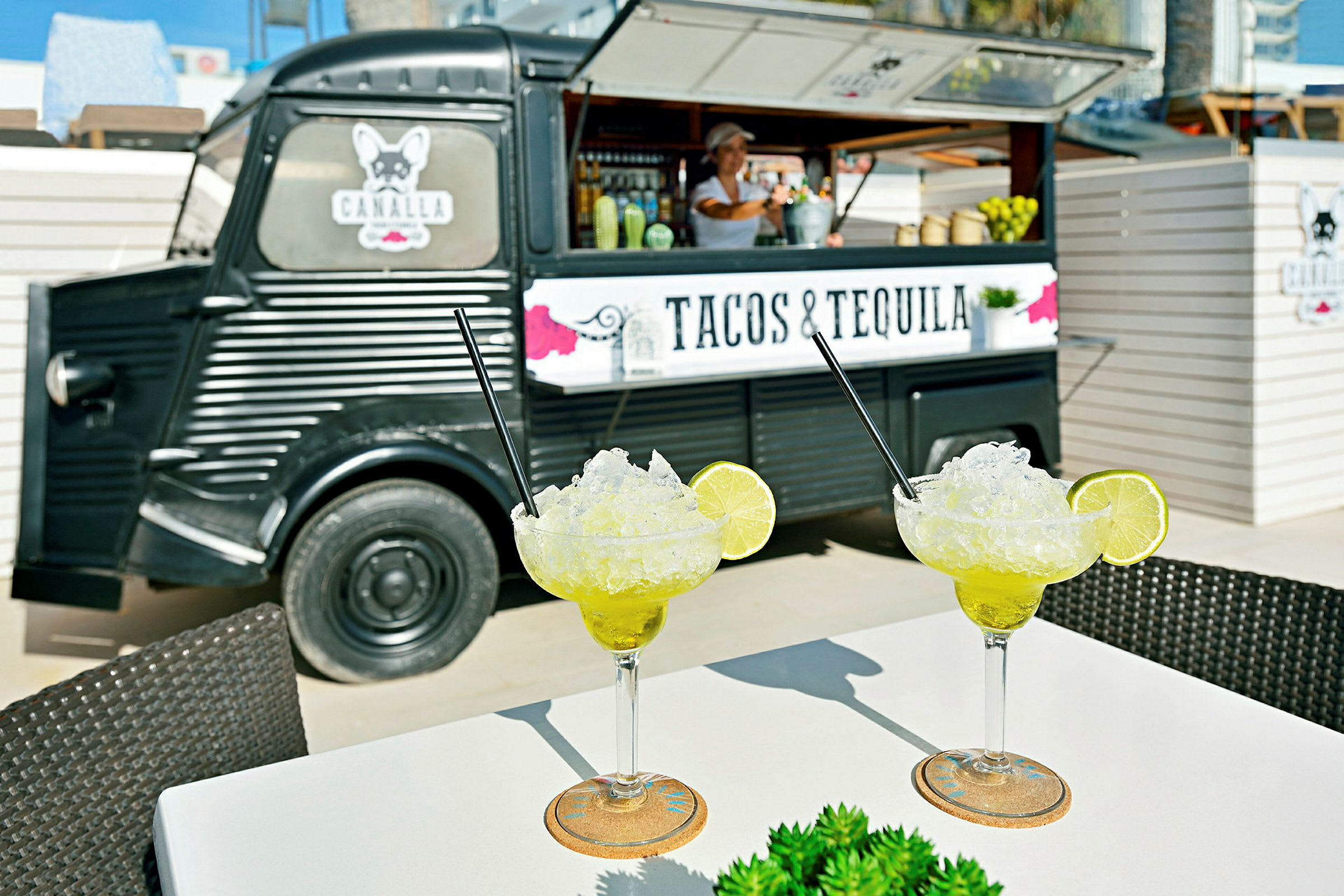 To glas margaritas står på et bord foran en madbil med teksten "Tacos & Tequila". (AI-genereret tekst)