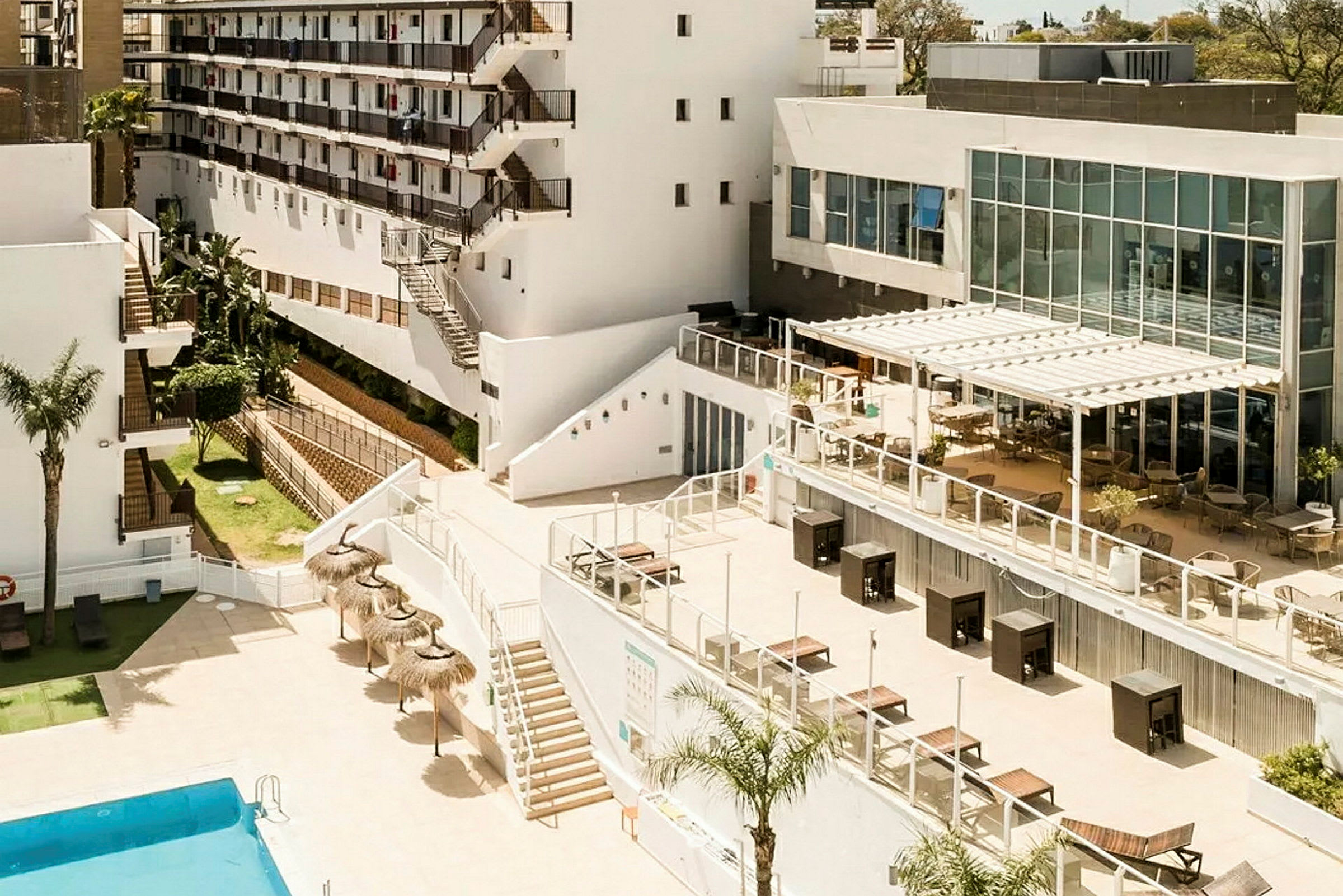 Billede af et hotelområde med pool, terrasse og hvide bygninger. (AI-genereret tekst)