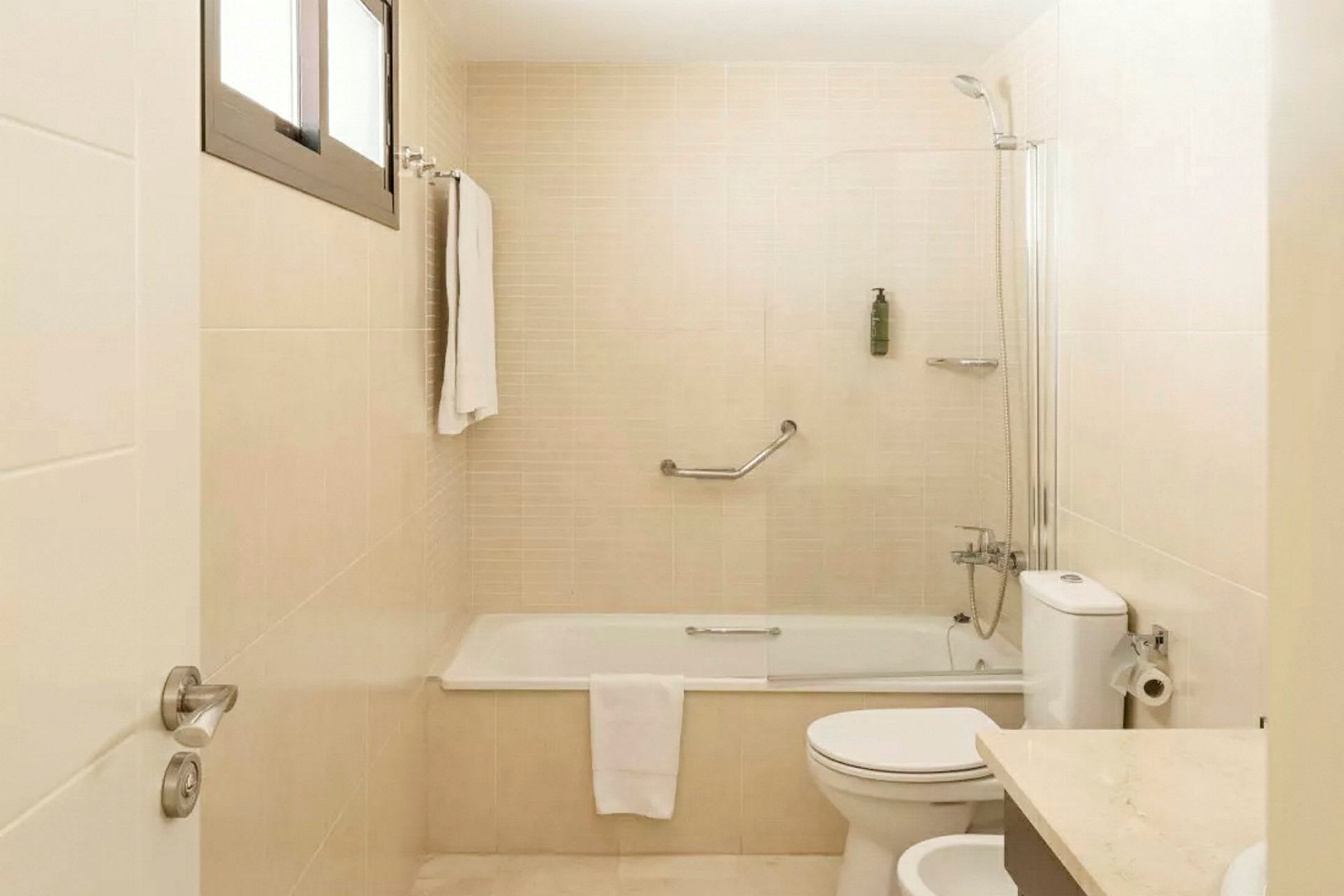 Et badeværelse med badekar, toilet og håndvask. Et håndklæde hænger på væggen. (AI-genereret tekst)