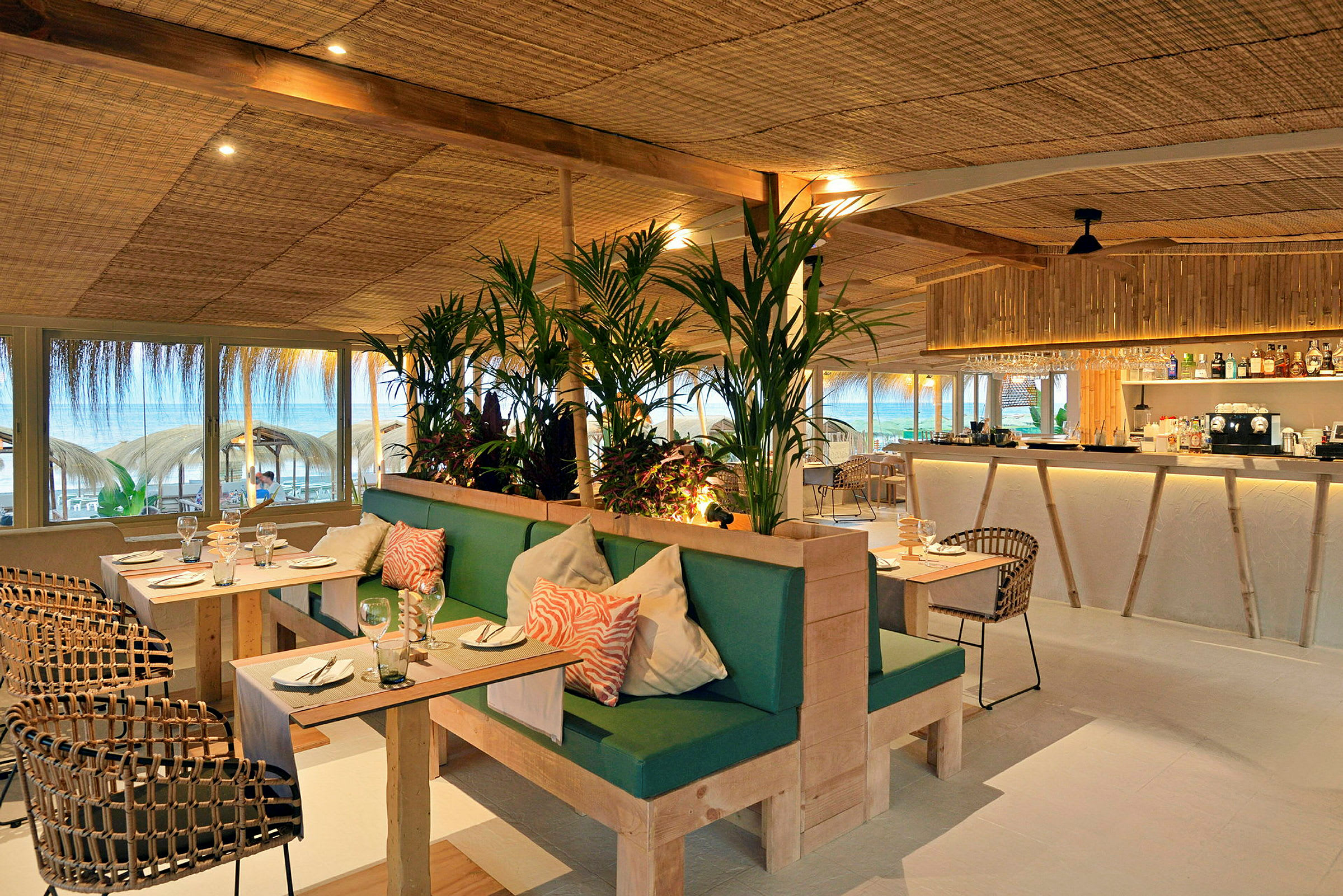 Restaurant med moderne indretning, grønne planter og udsigt til stranden. (AI-genereret tekst)