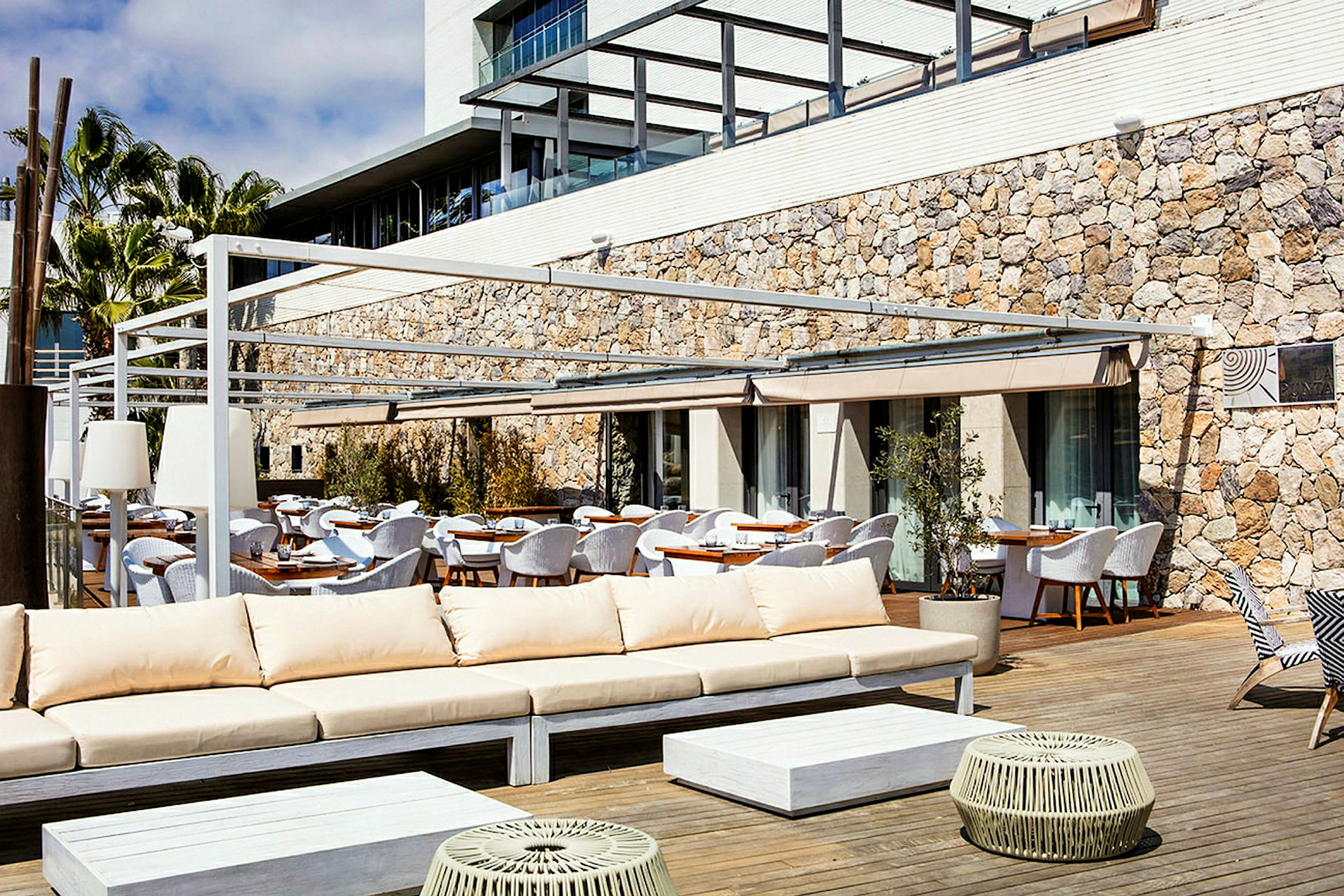 Udendørs loungemøbler og spiseborde på en terrasse med stenfacade i baggrunden. (AI-genereret tekst)
