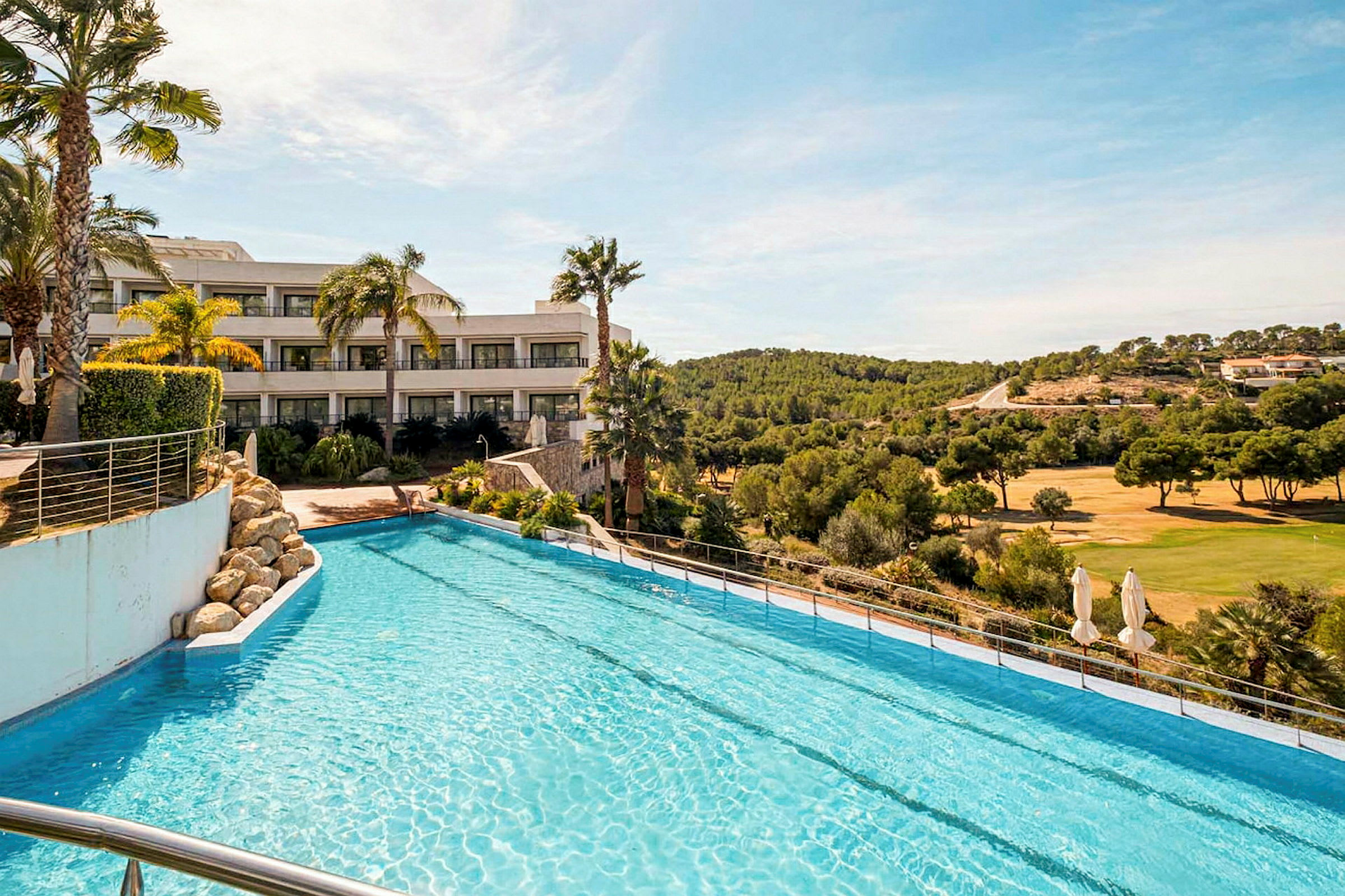 Et hotel ved en pool, med udsigt over et område med golf og skov i baggrunden. (AI-genereret tekst)