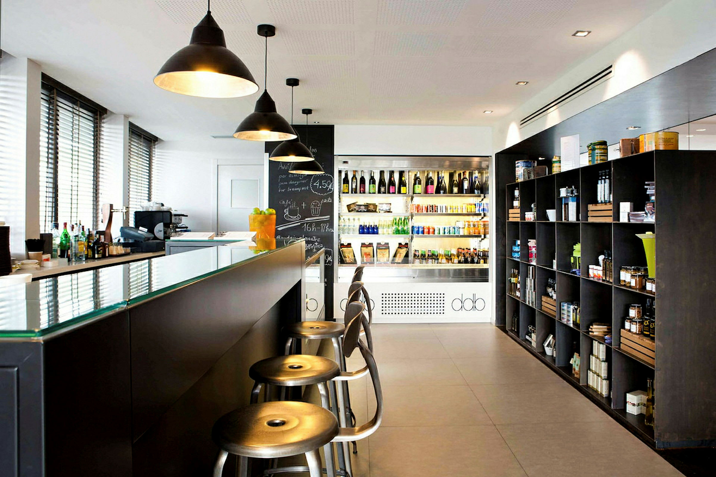 Et moderne caféområde med bardisk, hylder fyldt med diverse produkter og et køleskab med drikkevarer. (AI-genereret tekst)