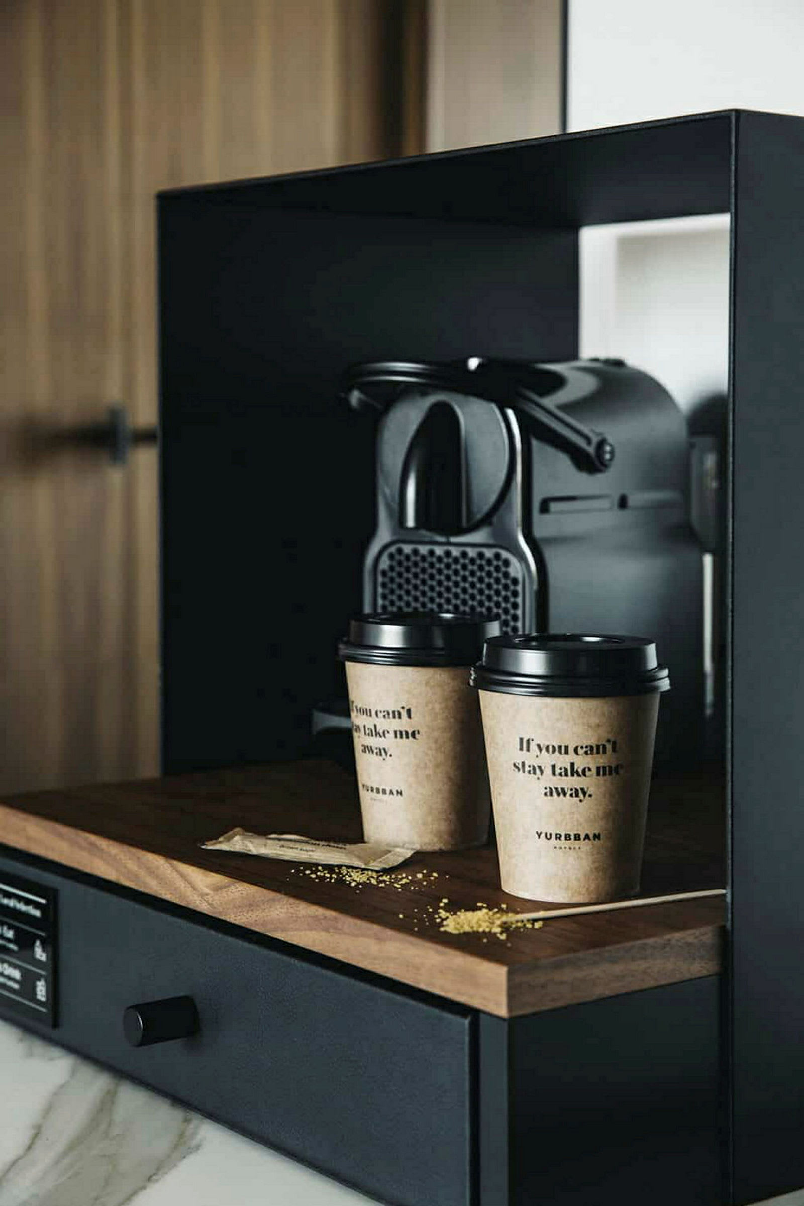 En kaffemaskine står på en mørk træbænk ved siden af to papkrus med kaffe. (AI-genereret tekst)