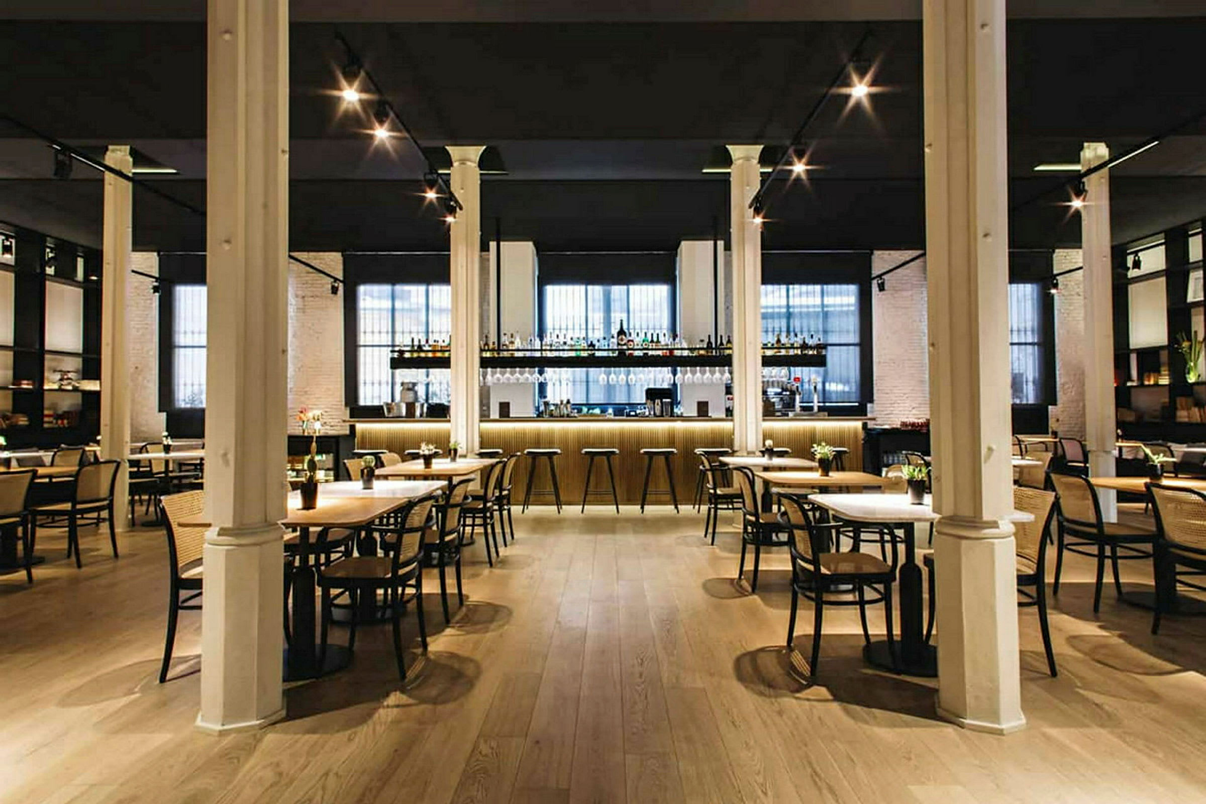En elegant restaurant med borde og stole samt en veloplyst bardisk i baggrunden. (AI-genereret tekst)