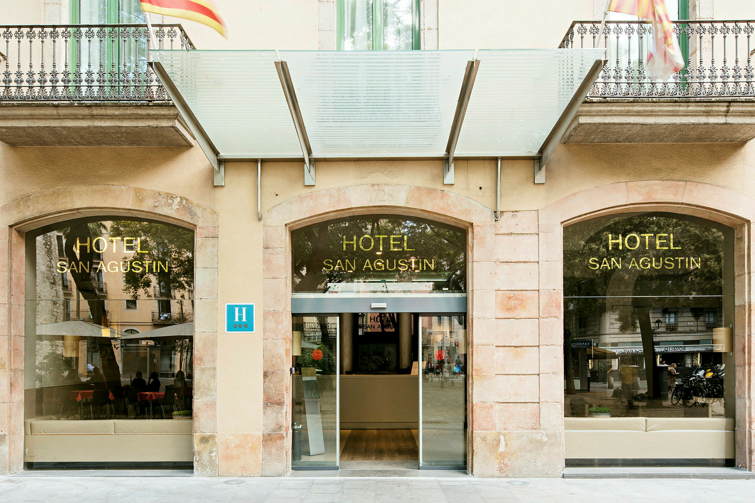 Hotelindgang med glasfacade og skilt med teksten 'HOTEL SAN AGUSTIN'. (AI-genereret tekst)