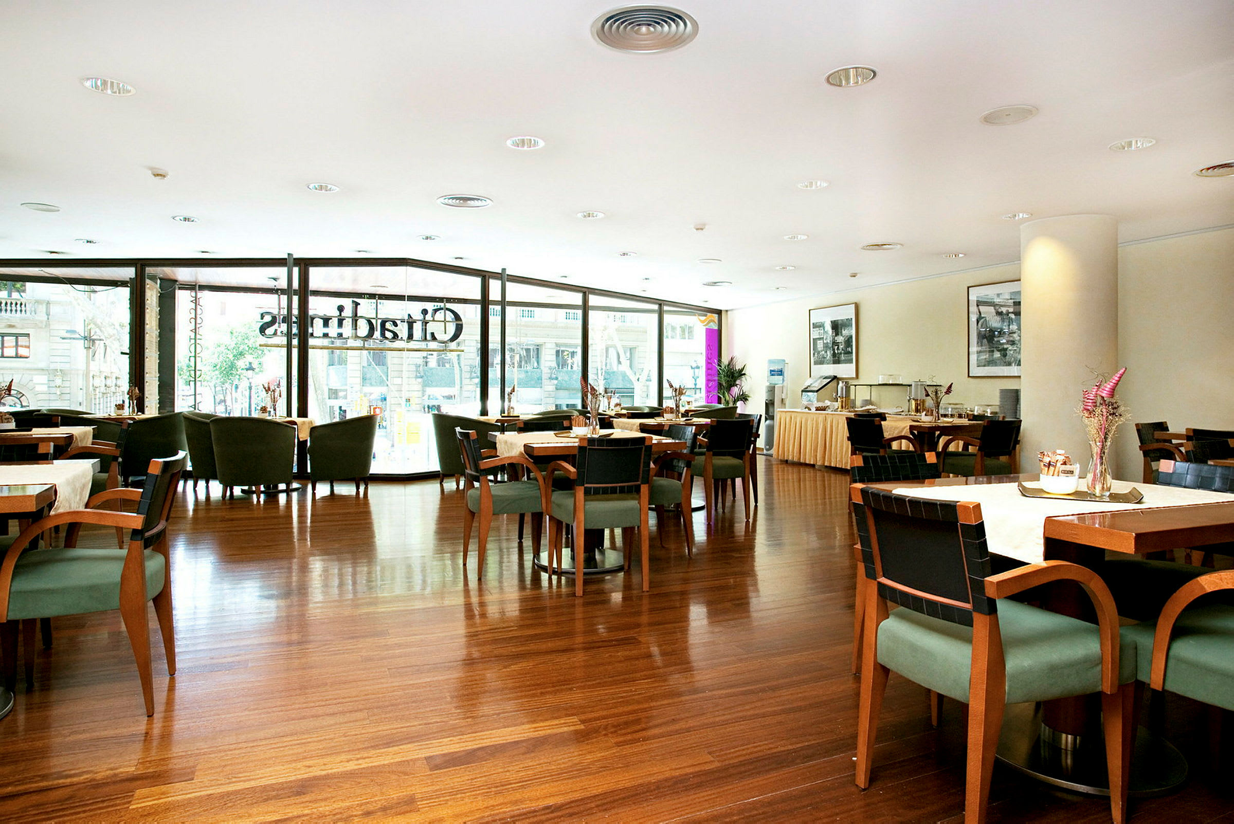 Et indendørsbillede af en elegant restaurant med borde og stole, hvor store vinduer lukker dagslys ind. (AI-genereret tekst)