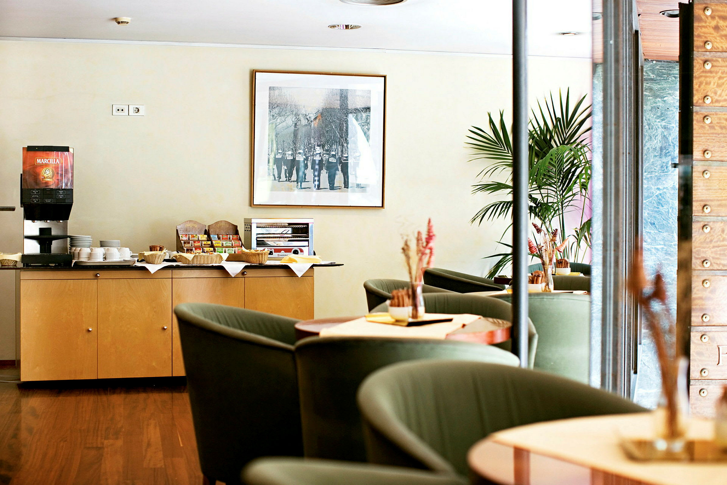 En kaffestation og siddeområde på et hotel eller café. En kaffemaskine og snacks er placeret på et skab. (AI-genereret tekst)