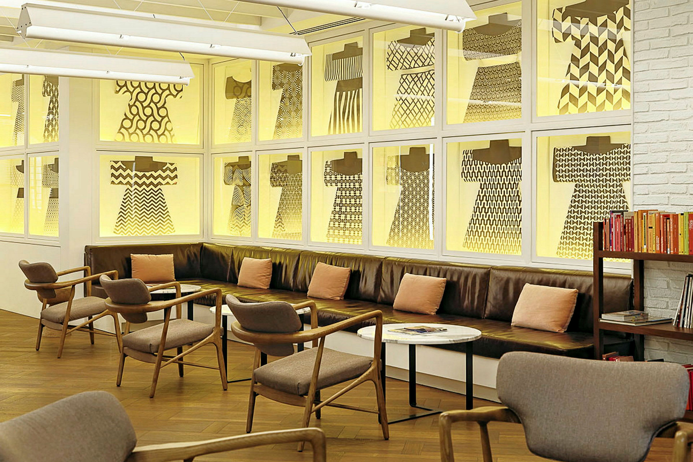 Interiør af en moderne lounge med lædersofaer og træstole, samt hylder med bøger. Væggene prydet med mønstrede gennemsigtige billeder. (AI-genereret tekst)