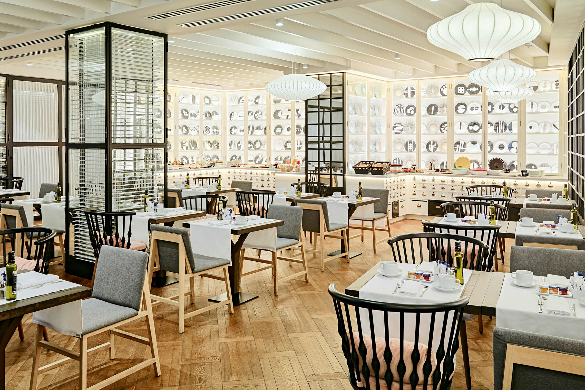 Et elegant indrettet restaurantområde med moderne møbler, hvide vægge dekoreret med dekorative genstande og hyggelig belysning. (AI-genereret tekst)