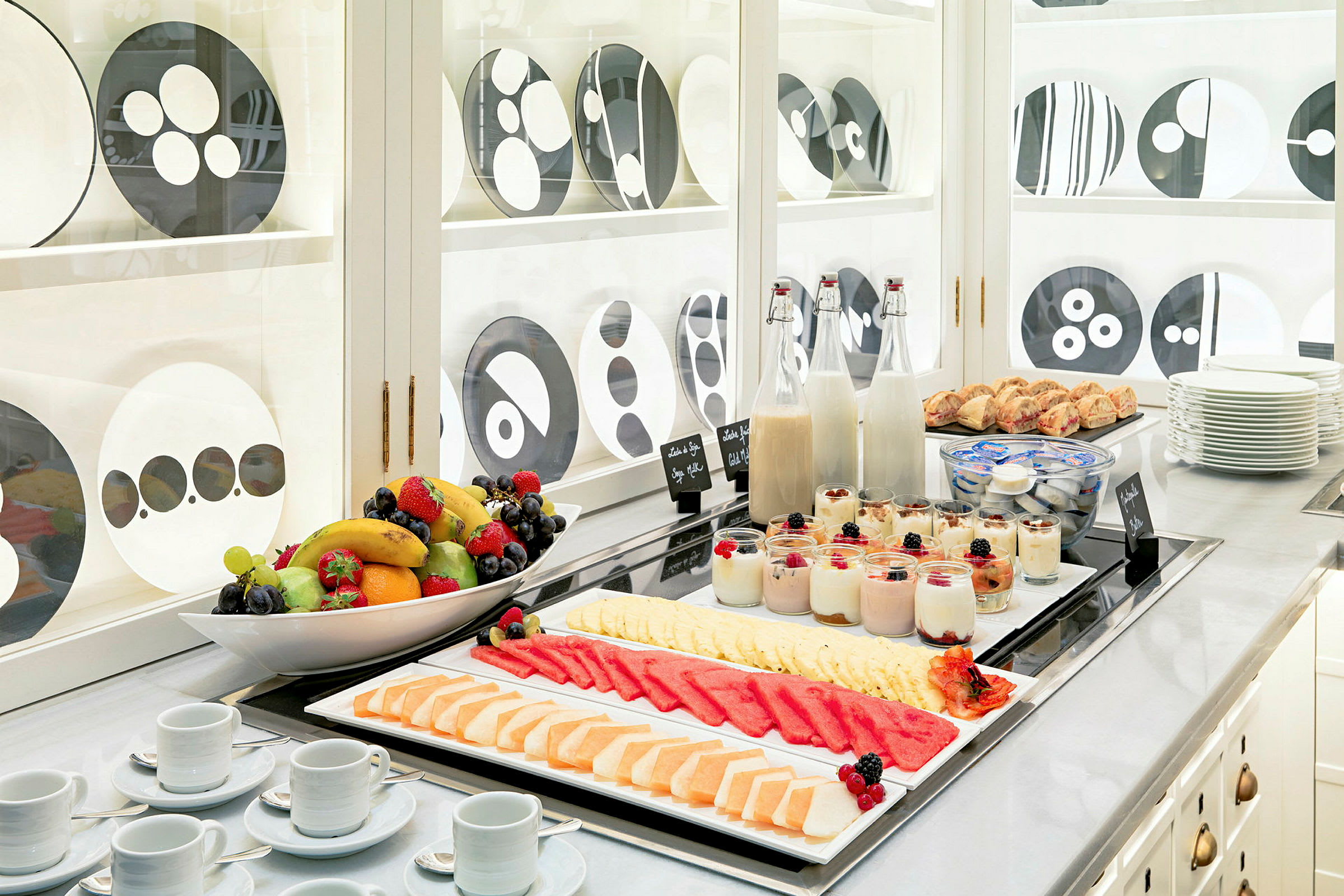 Morgenbuffet med frisk frugt, yoghurt, juice og bagværk på et bord. (AI-genereret tekst)